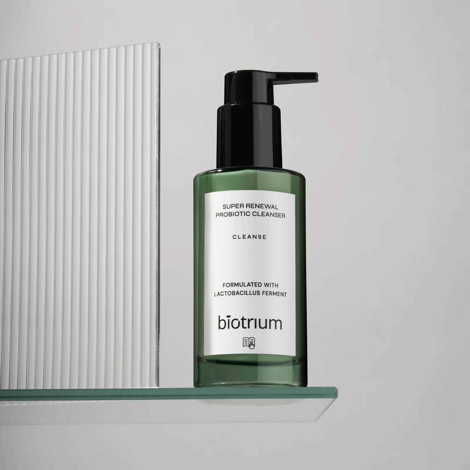 Green Biotrium cleanser bottle on a glass shelf beside a ribbed white panel.