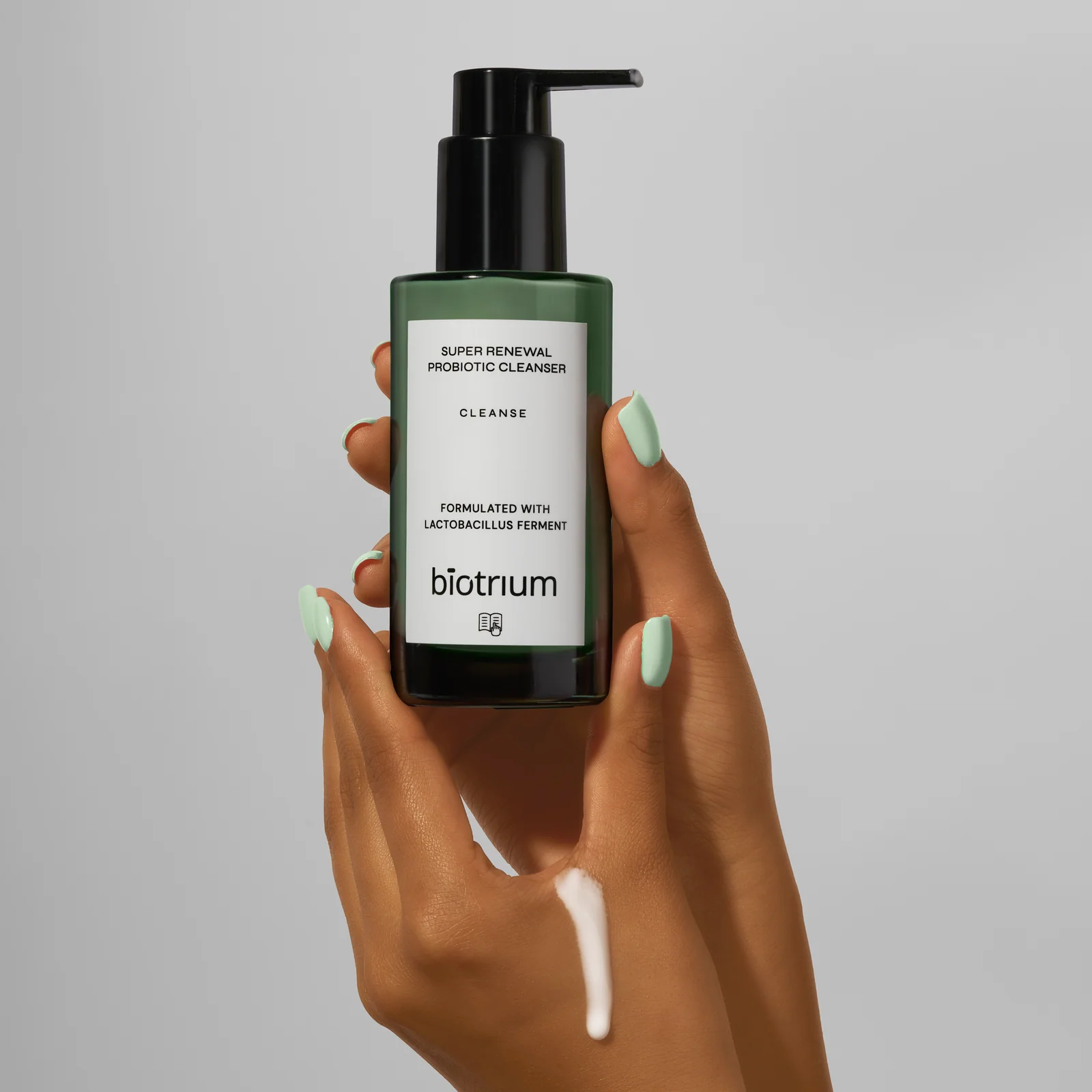 Hands holding a green Biotrium cleanser bottle with a streak of cream on the skin.