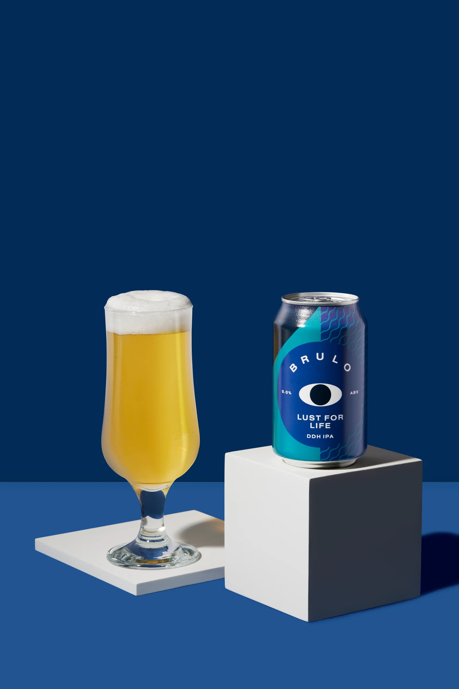 Brülo can and a filled beer glass on white platforms against a blue background.