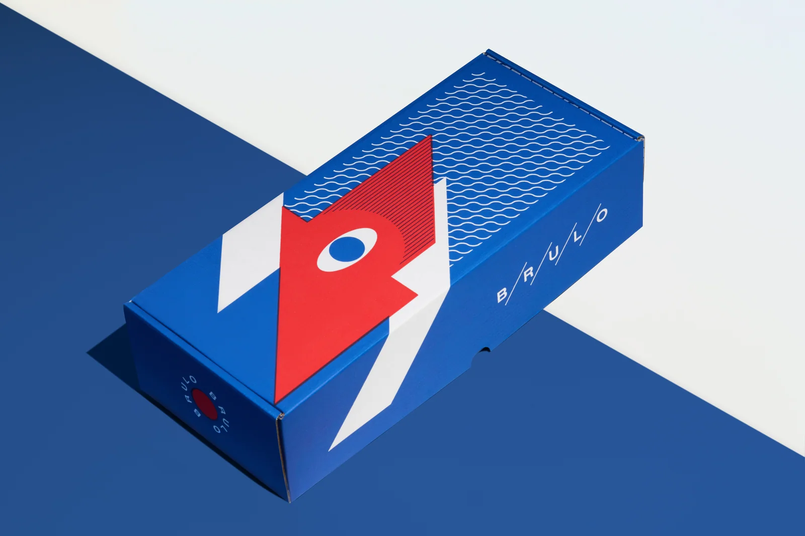 Closed blue Brülo gift box with red-and-white graphics on a blue-and-white surface.