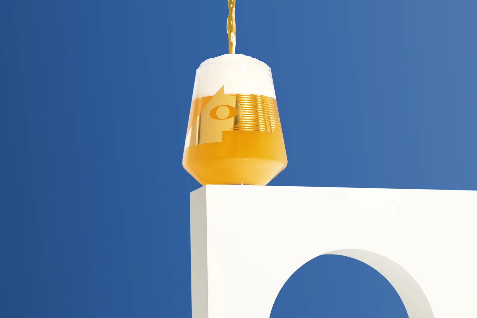Beer pouring into a Brülo glass on a white architectural plinth against blue.