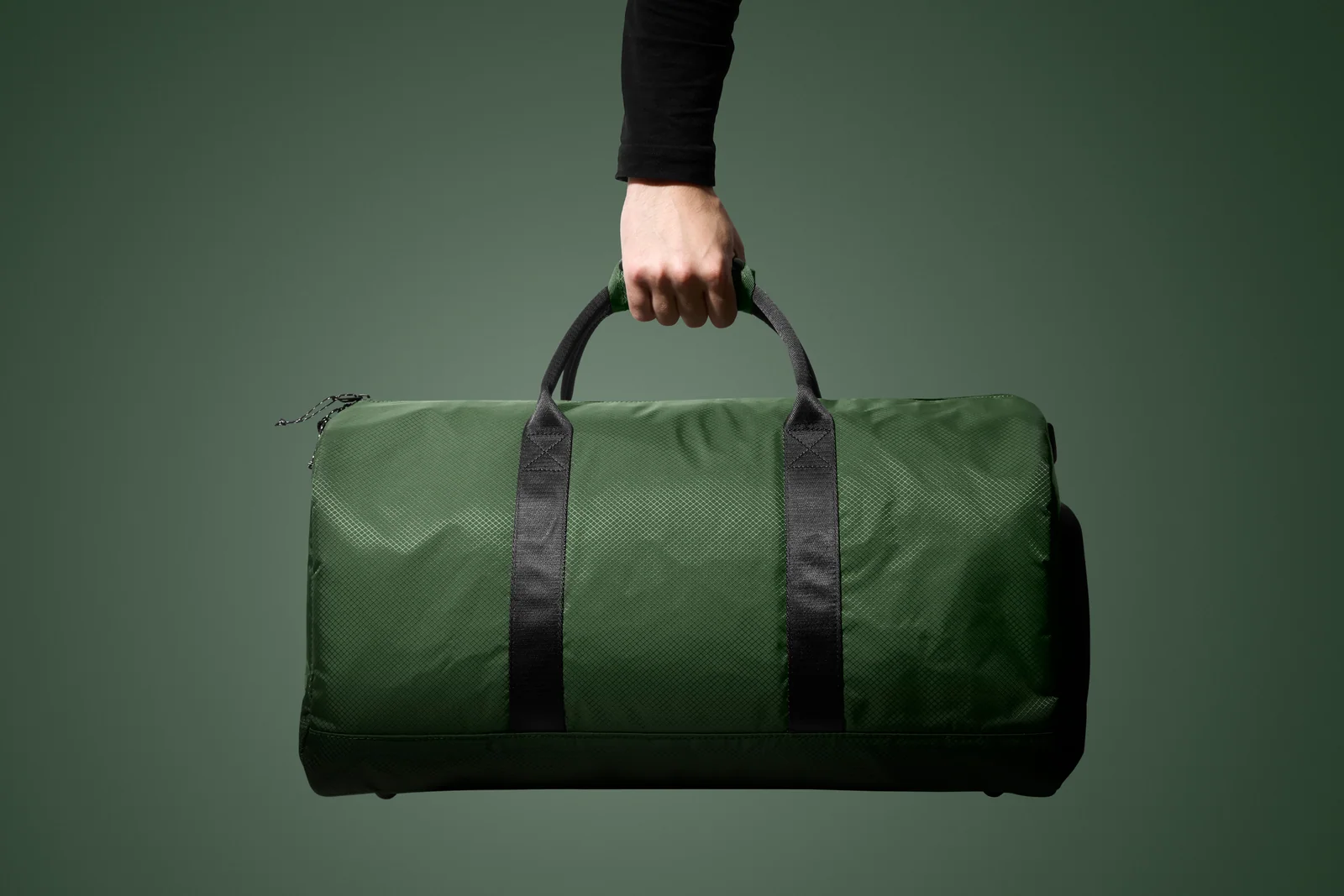 Hand holding a green Double Oak duffel bag by its handles against green.