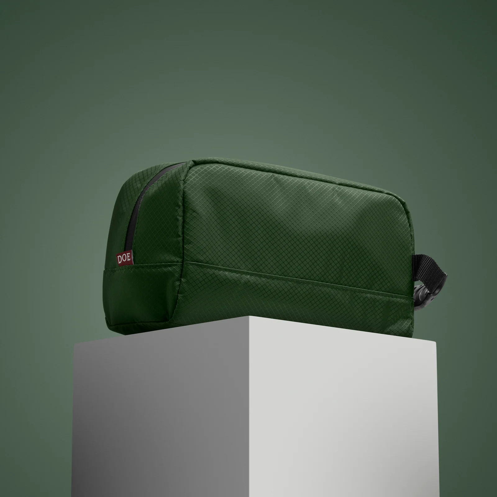 Green Double Oak zip pouch on a white plinth against a green background.
