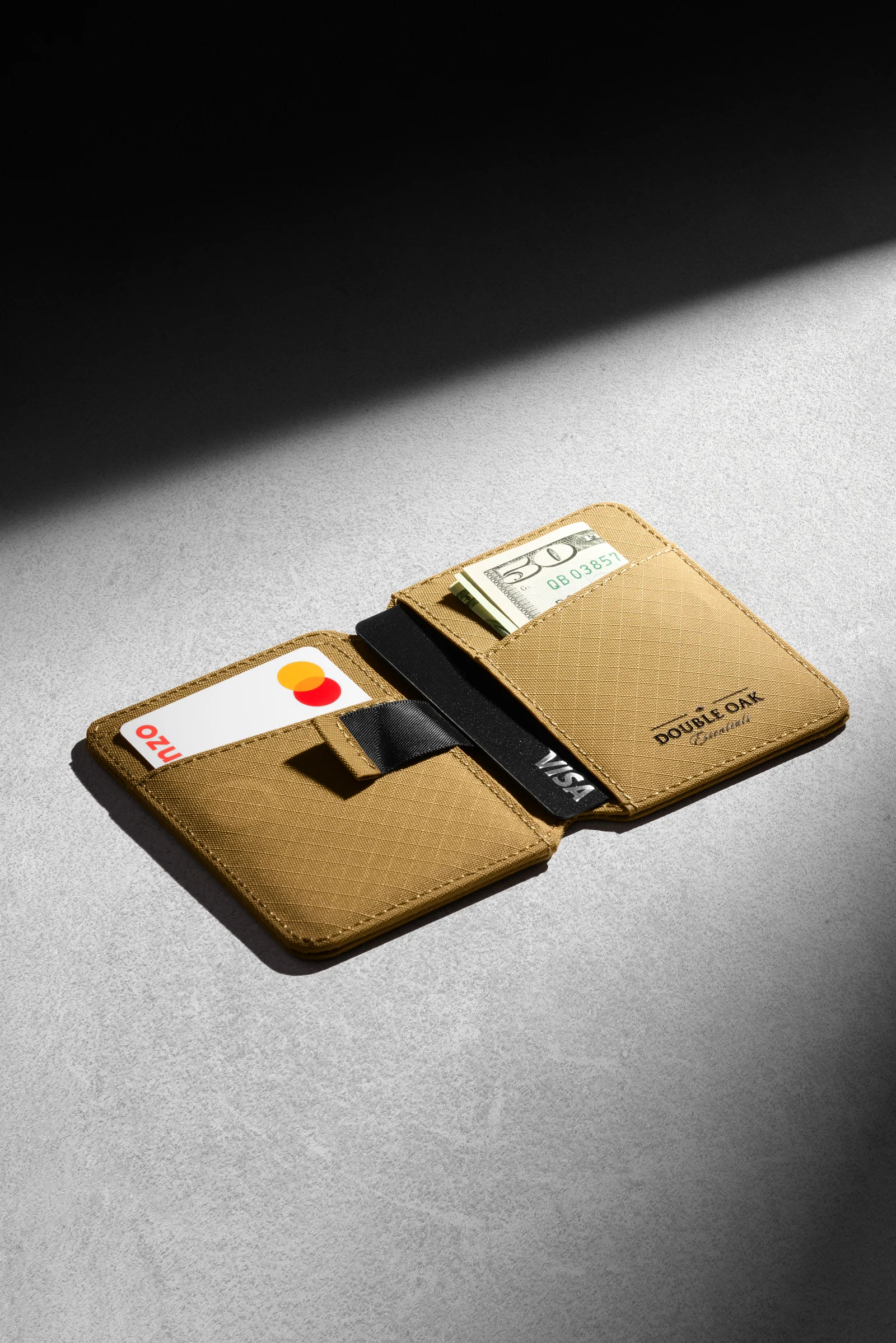 Open tan Double Oak wallet with cards and a banknote on grey in directional light.