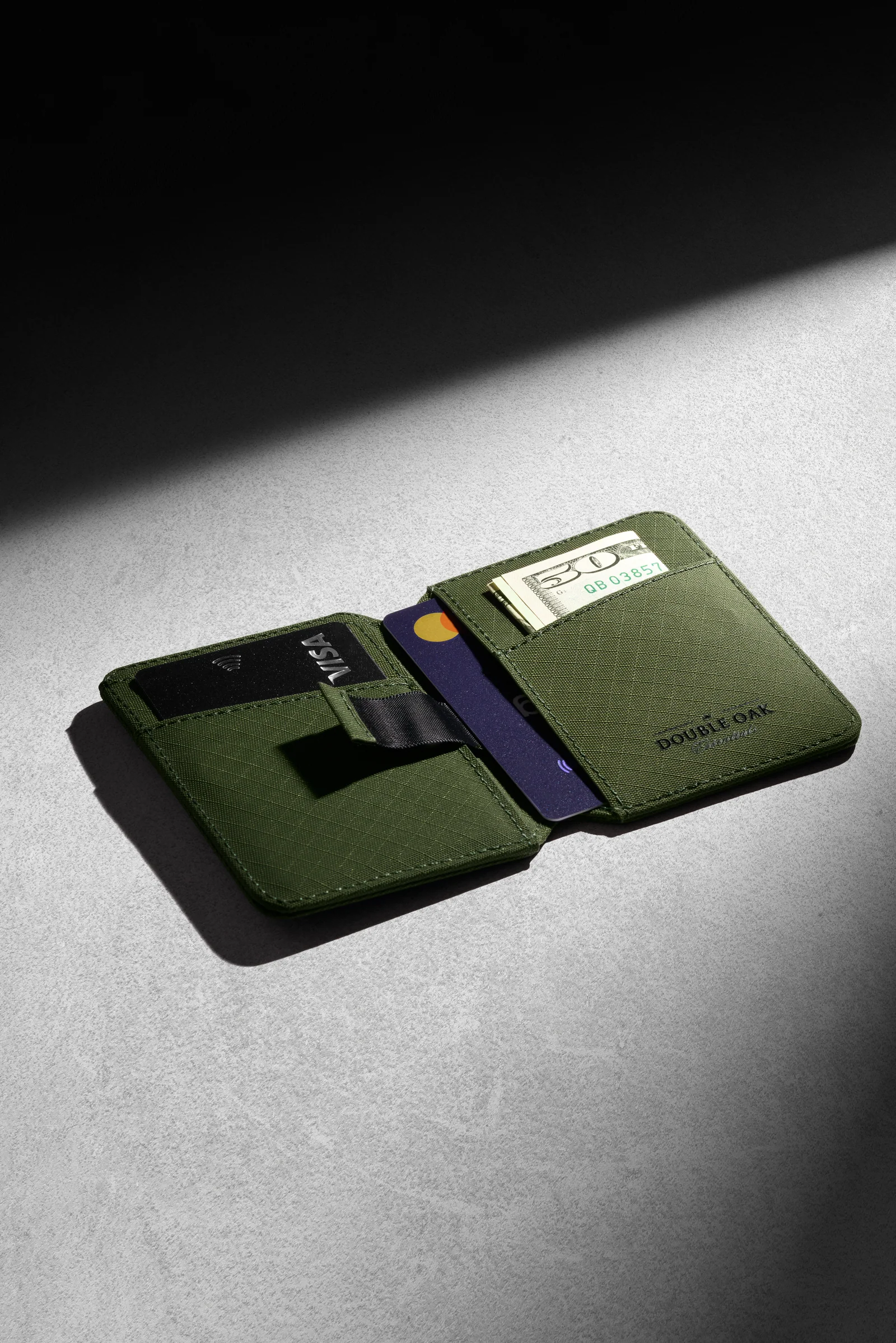 Open olive-green Double Oak wallet with cards and a banknote on grey in directional light.
