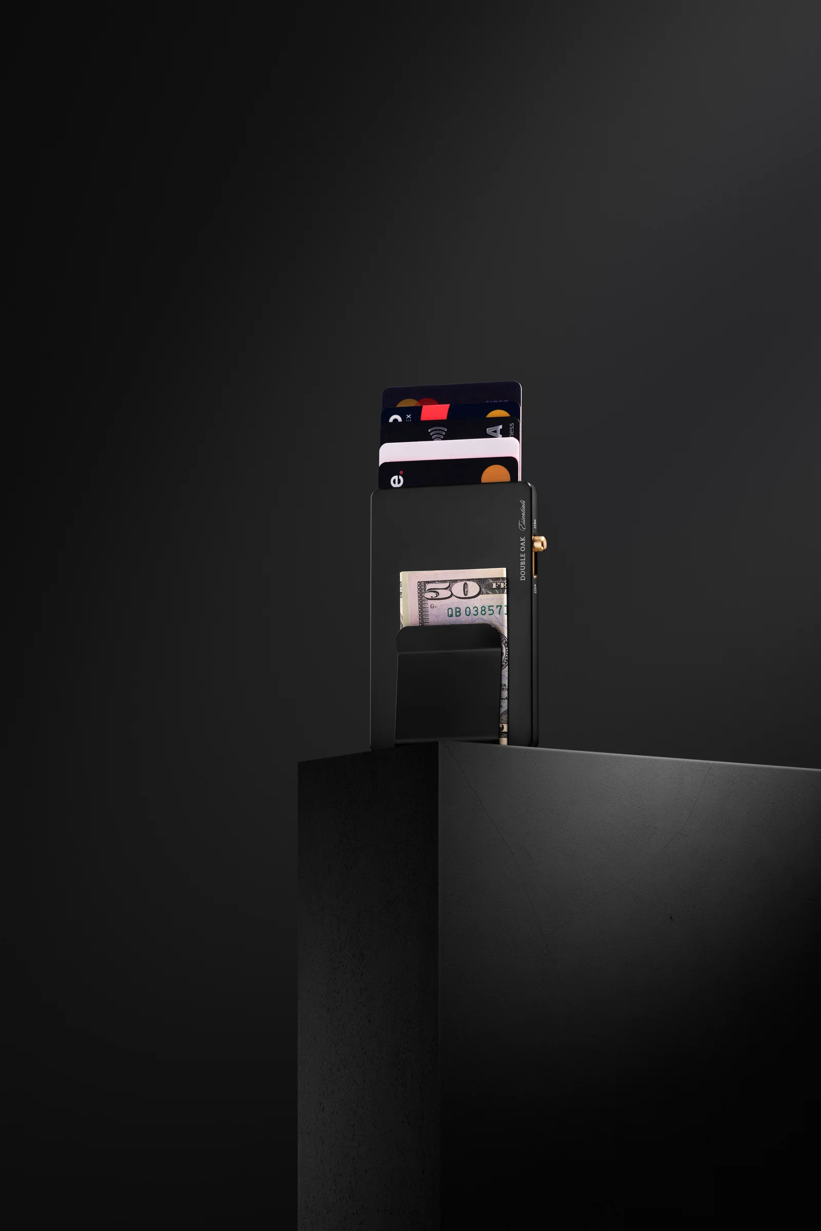 Black Double Oak cardholder with raised cards and a banknote on a dark plinth.