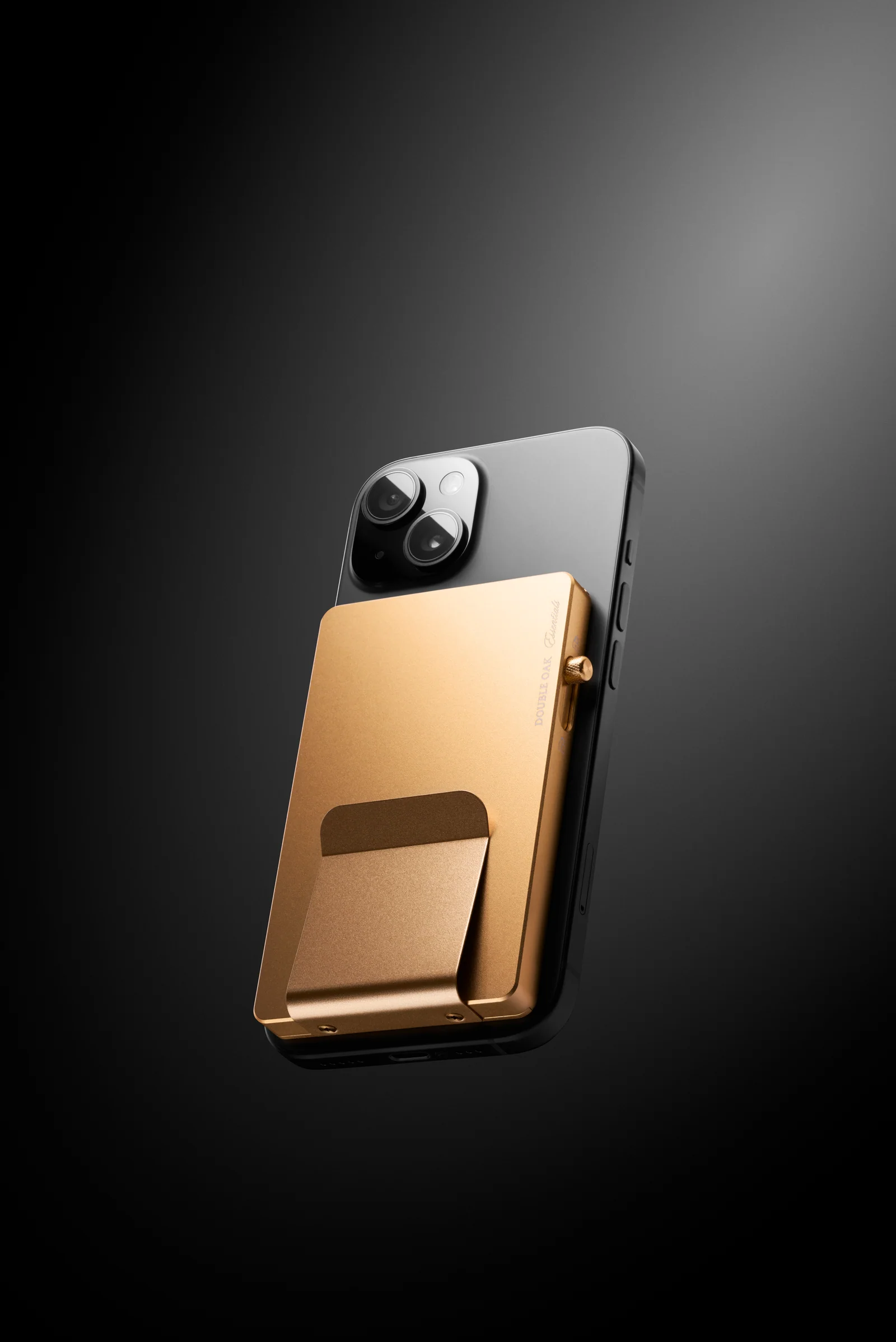Gold-coloured Double Oak cardholder attached to the back of a phone against a dark background.