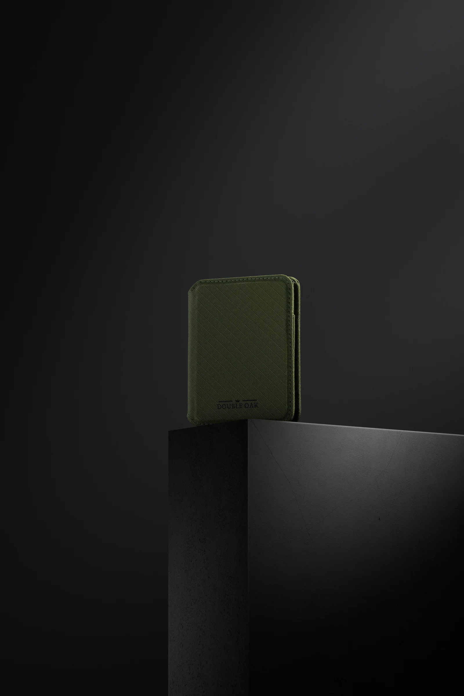 Closed green Double Oak wallet standing on a dark plinth.