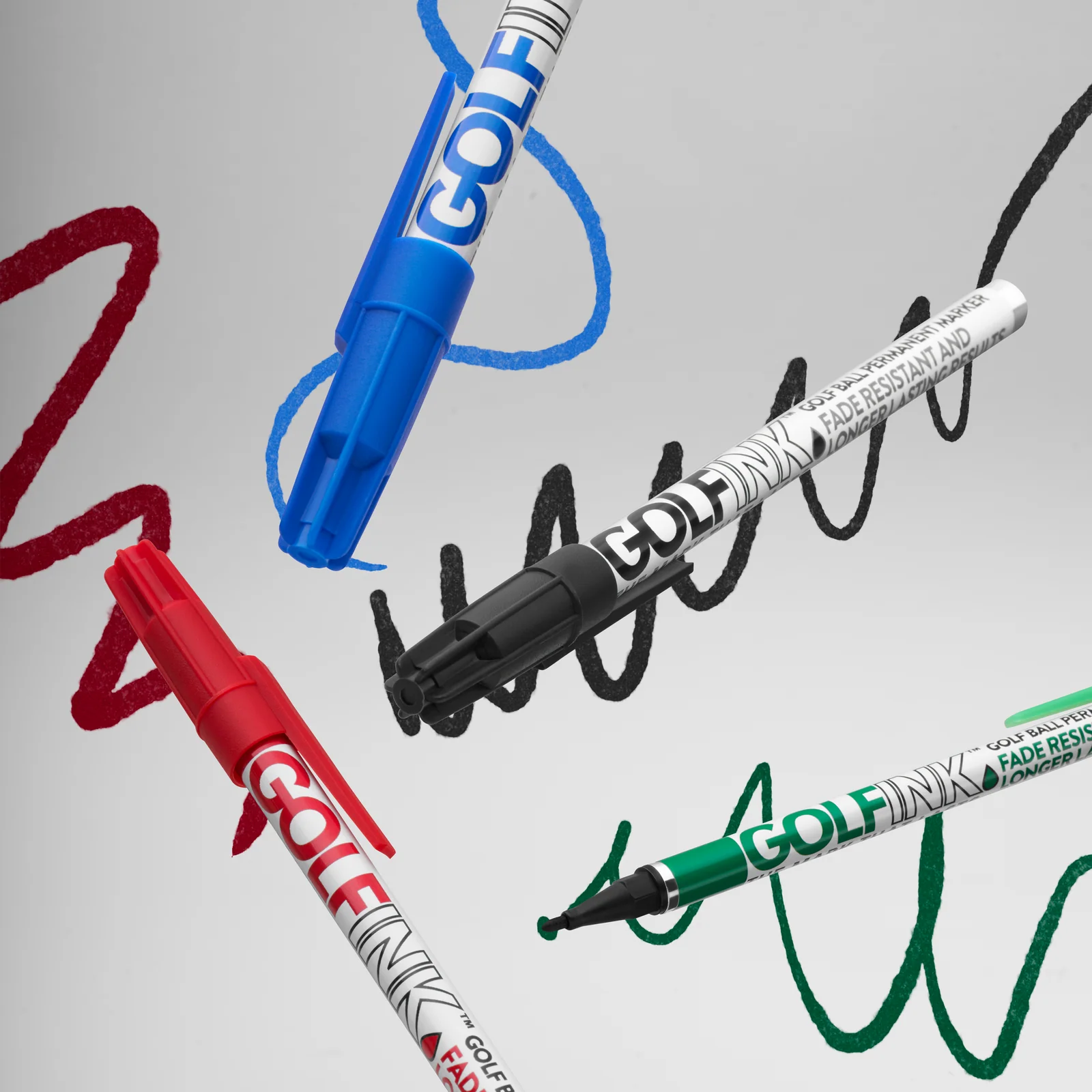 Blue, black, red and green Golf Ink pens arranged over matching ink strokes on a light background.