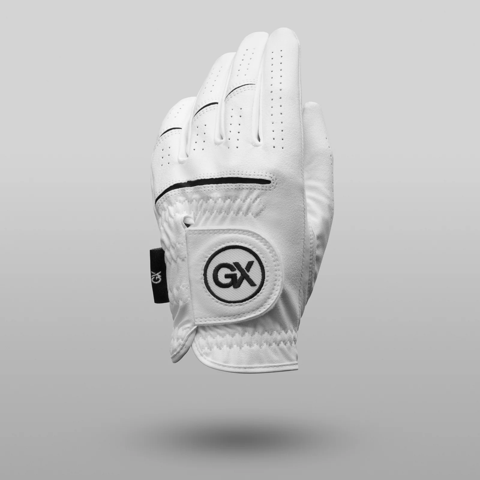 White GX Golf glove with black trim and a round logo patch suspended above a soft shadow on grey.