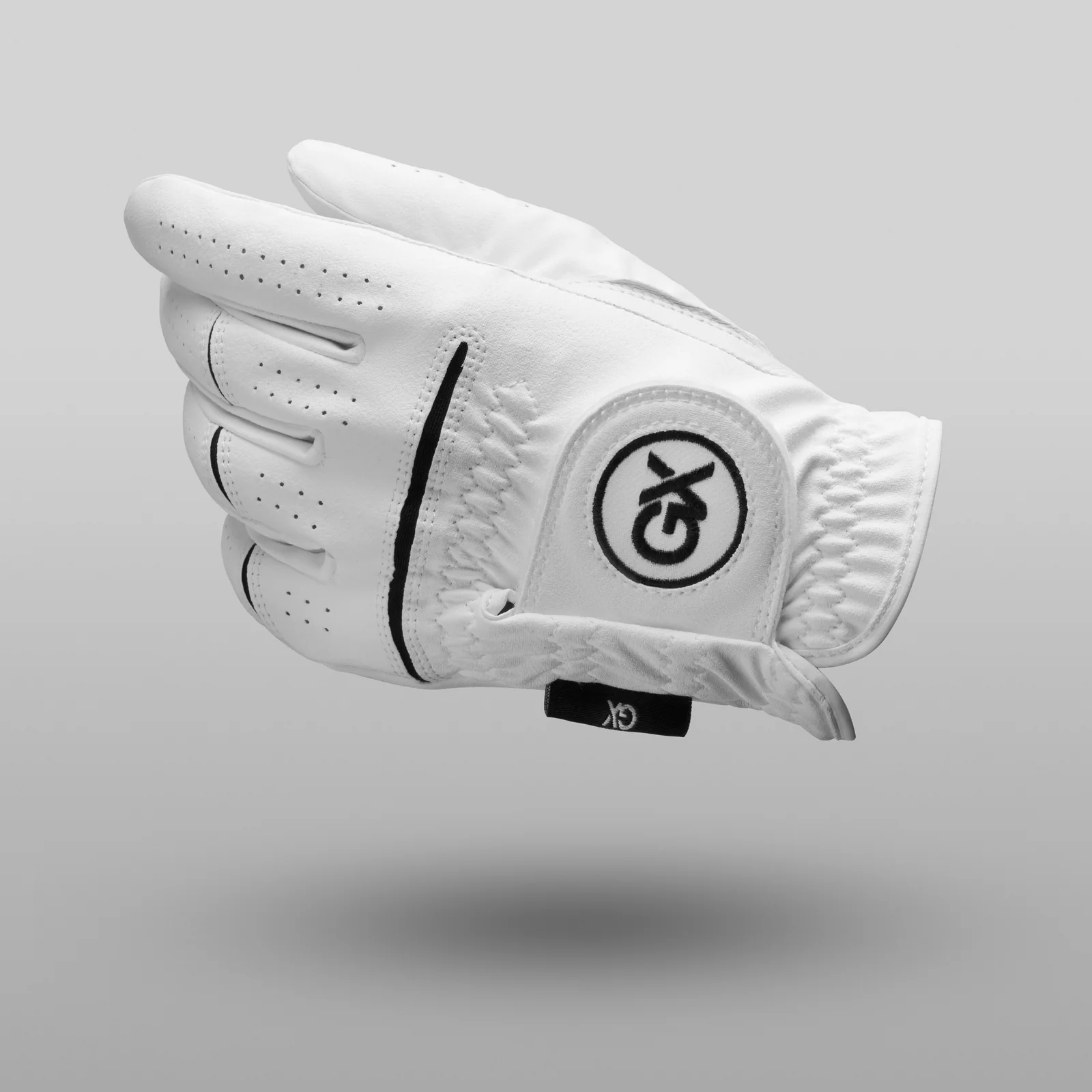 Curved white GX Golf glove with black trim and a round logo patch shown from the back above a soft shadow on grey.