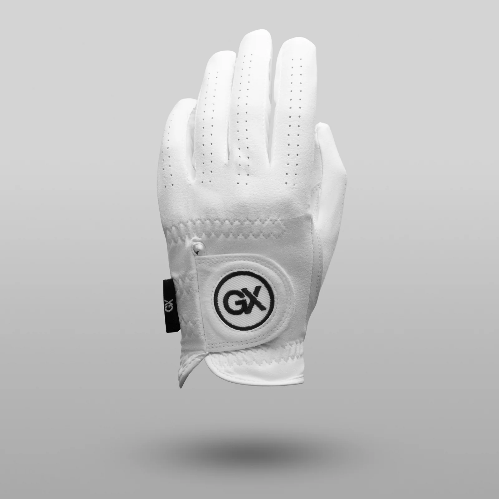 Straight-on rear view of a white GX Golf glove with perforated fingers and a round logo patch above a soft shadow on grey.
