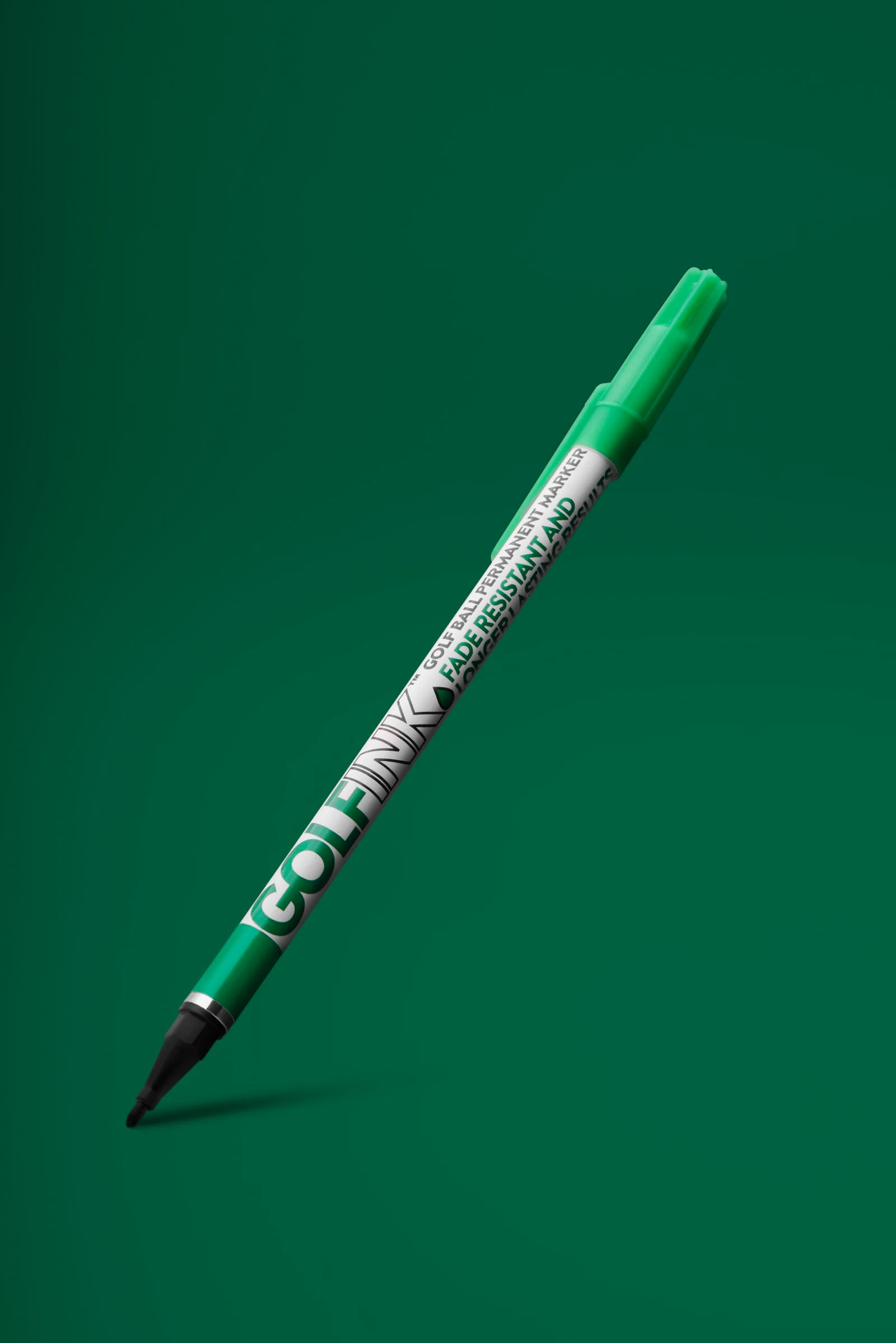 Green Golf Ink ball-marking pen angled above a soft shadow against green.