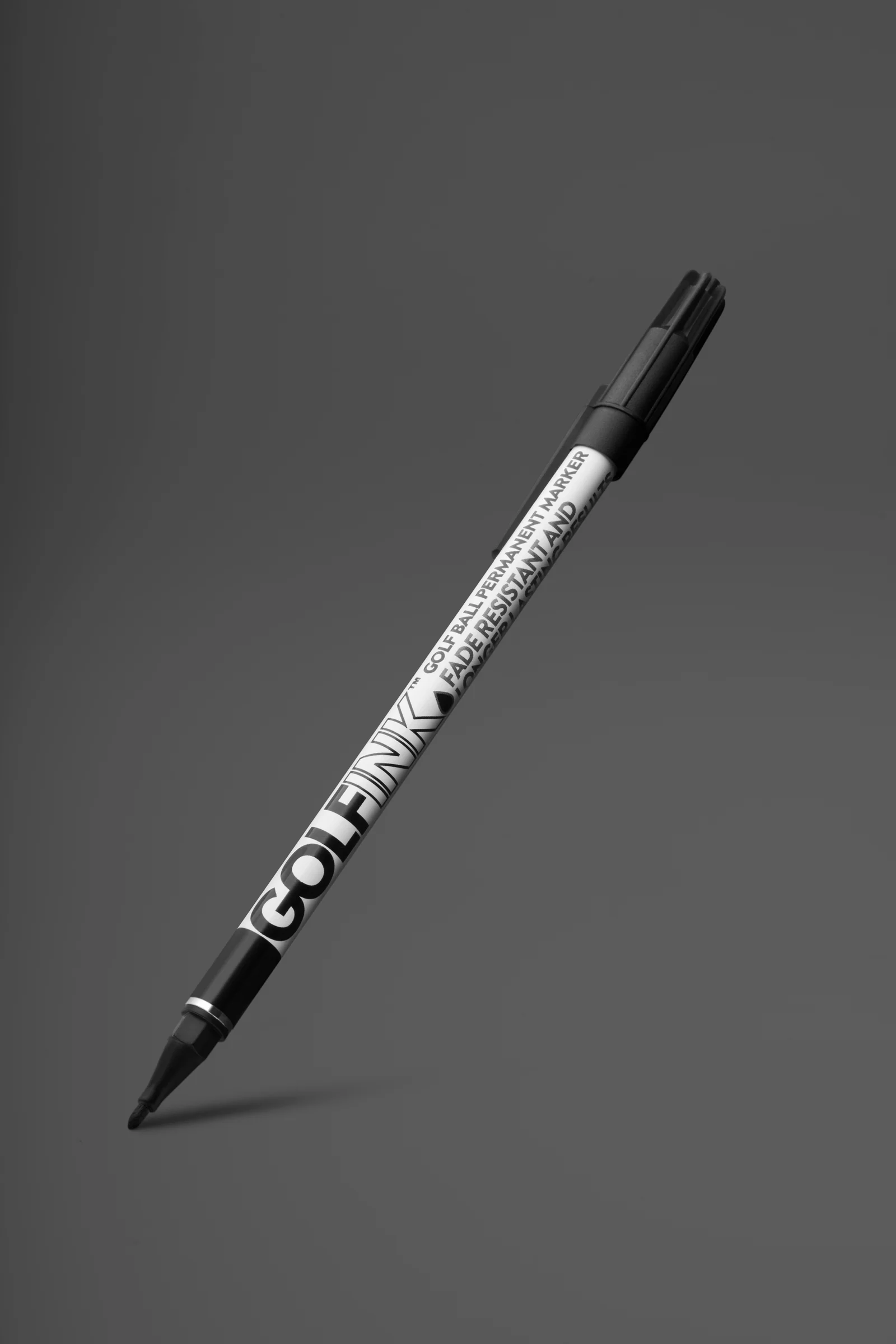 Black Golf Ink ball-marking pen angled above a soft shadow against grey.