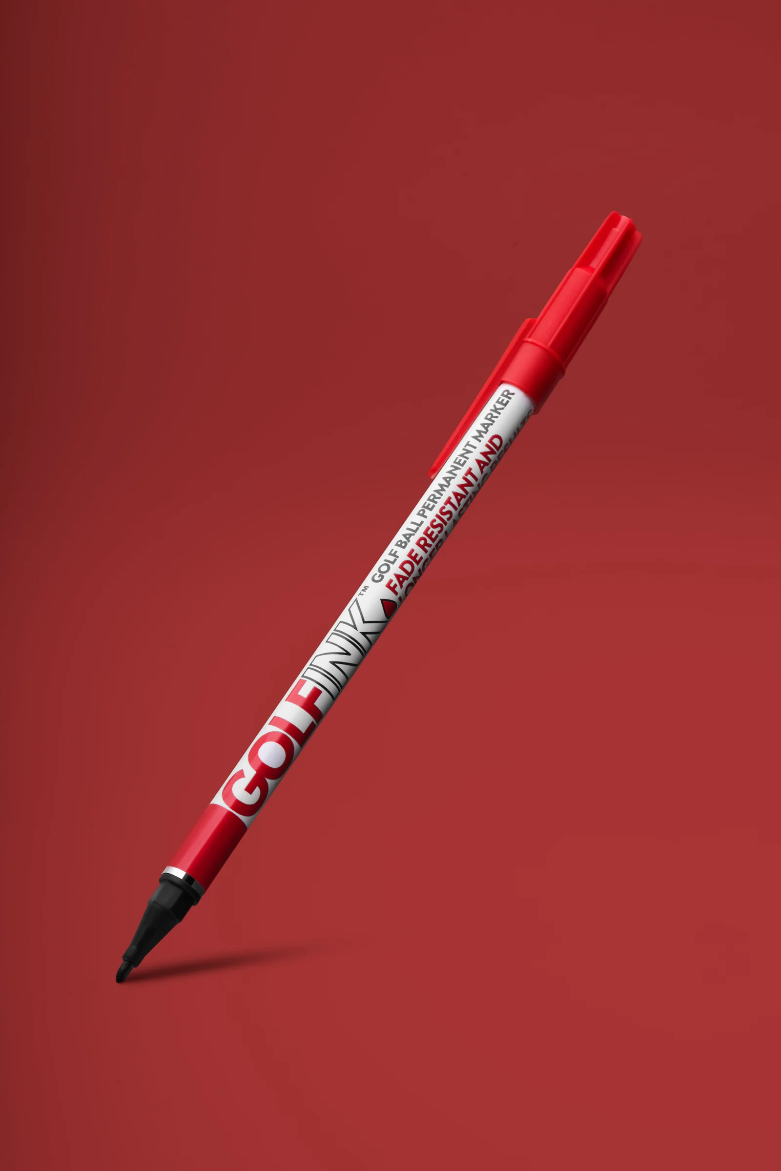 Red Golf Ink ball-marking pen angled above a soft shadow against red.