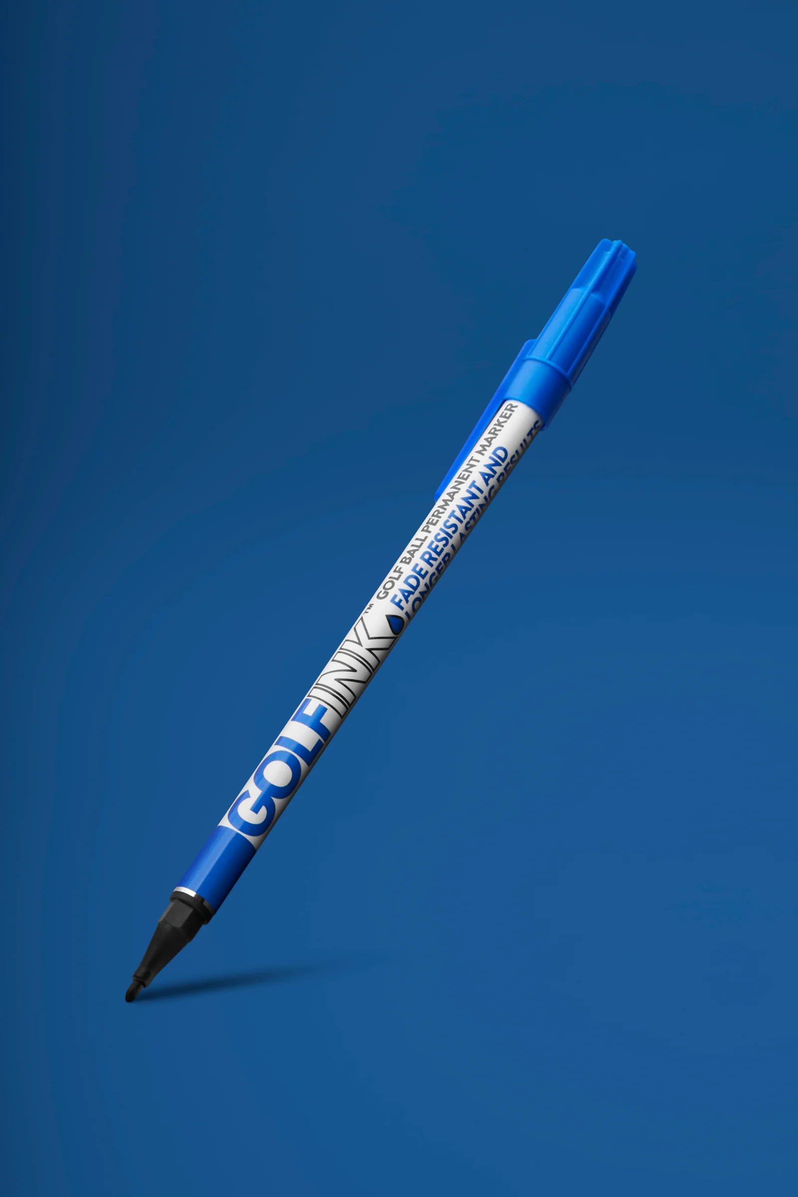 Blue Golf Ink ball-marking pen angled above a soft shadow against blue.