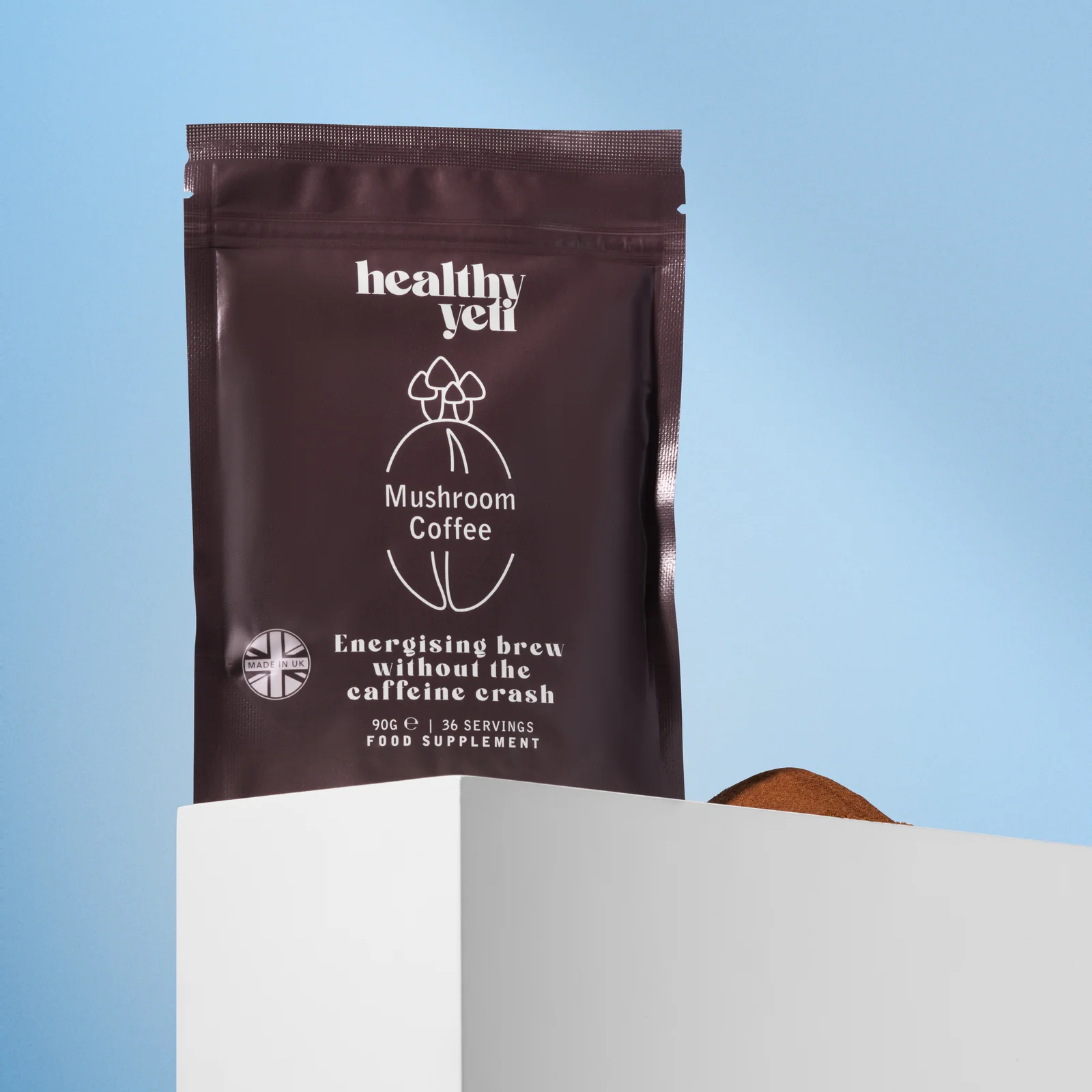 Healthy Yeti Mushroom Coffee pouch and a mound of powder behind a white plinth against blue.