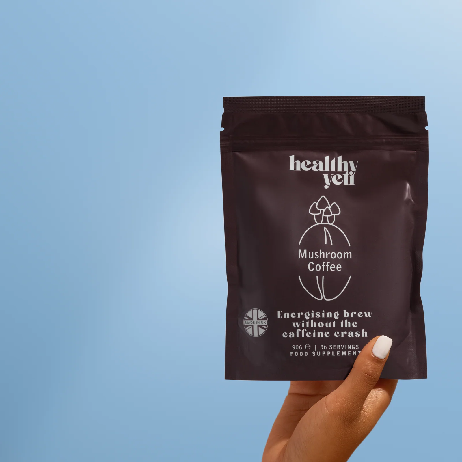 Hand holding a brown Healthy Yeti Mushroom Coffee pouch against blue.