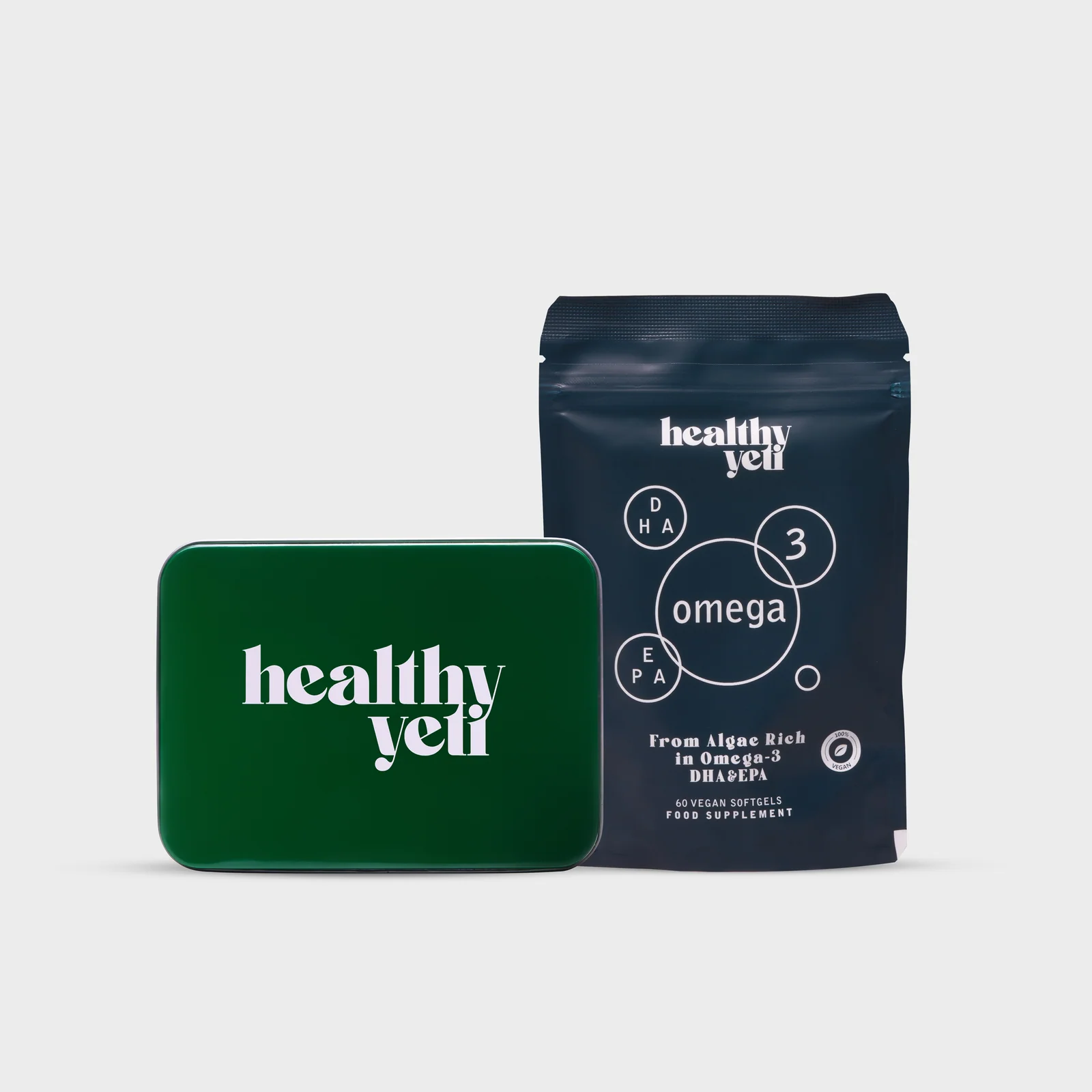 Closed green Healthy Yeti tin beside a blue Omega 3 pouch on a light background.