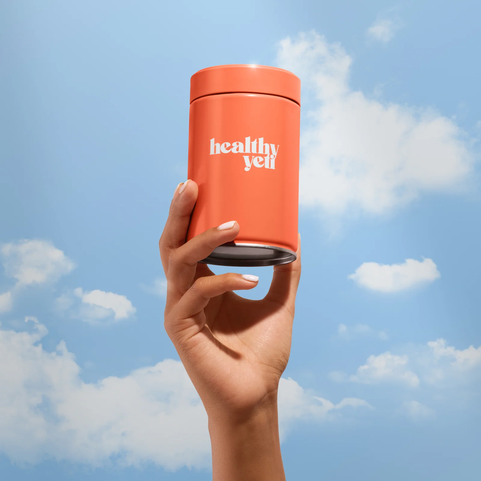 Hand holding an orange Healthy Yeti jar against a blue sky with clouds.