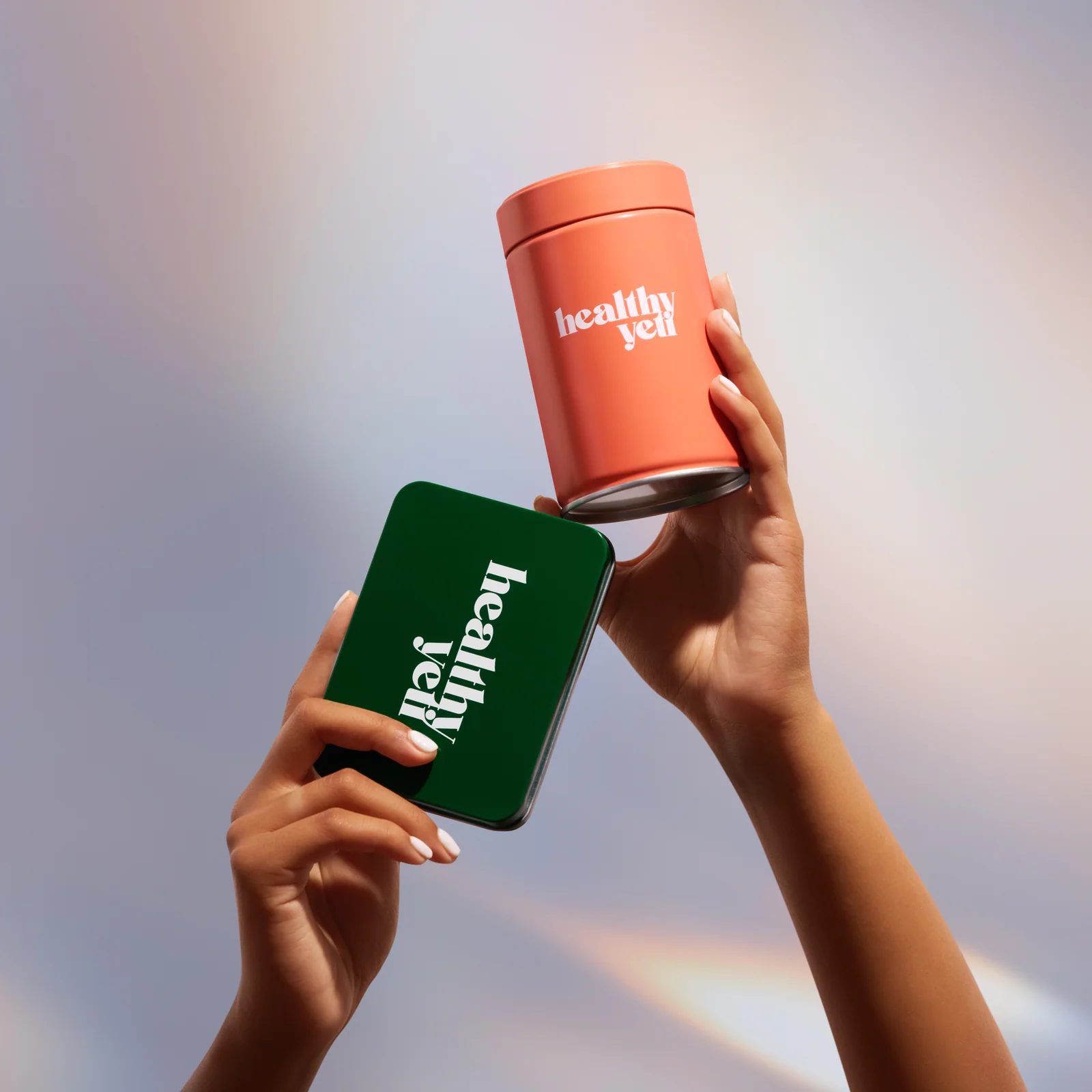 Hands holding an orange Healthy Yeti jar and a green branded tin against an iridescent background.