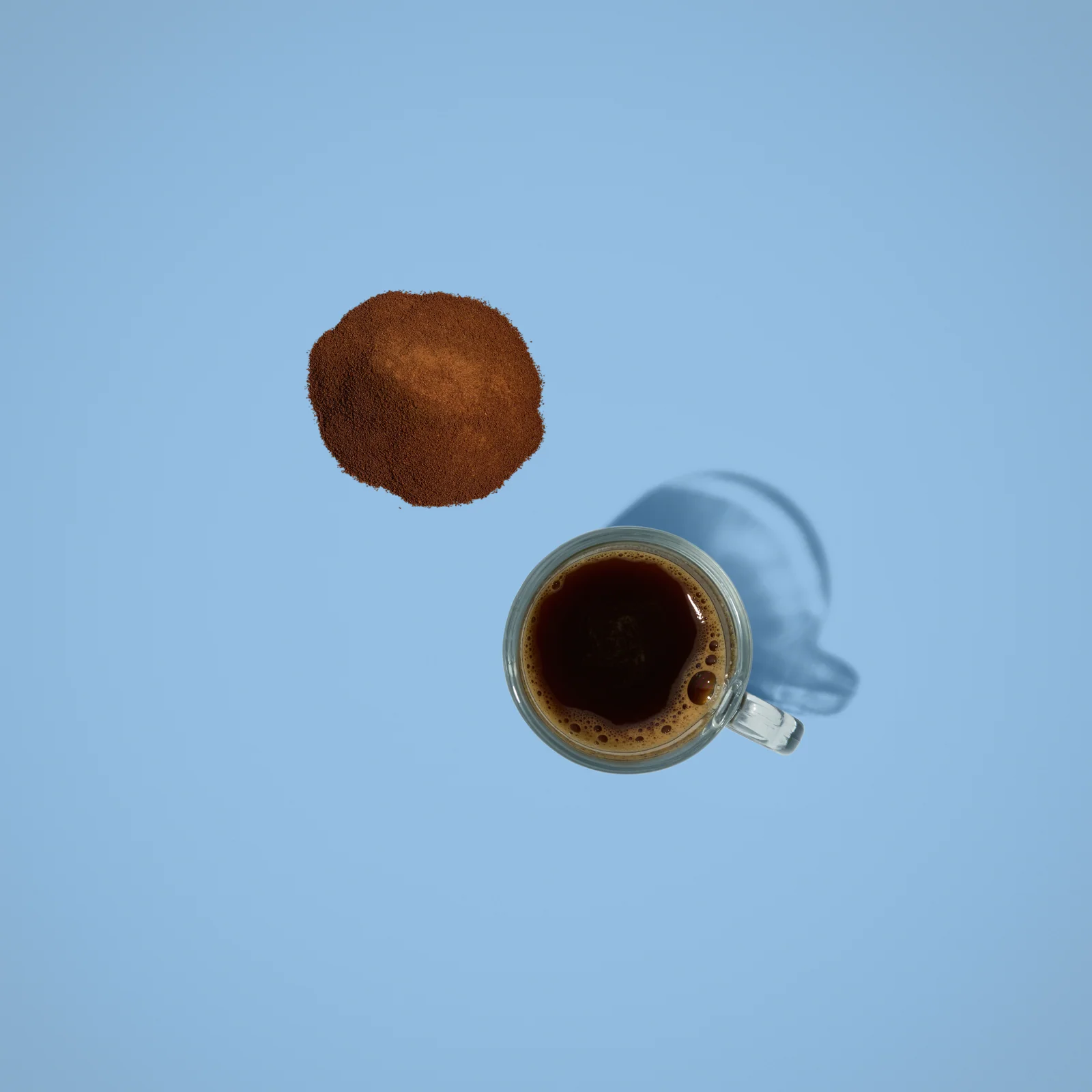 Overhead view of a cup of black coffee and a mound of powder against blue.