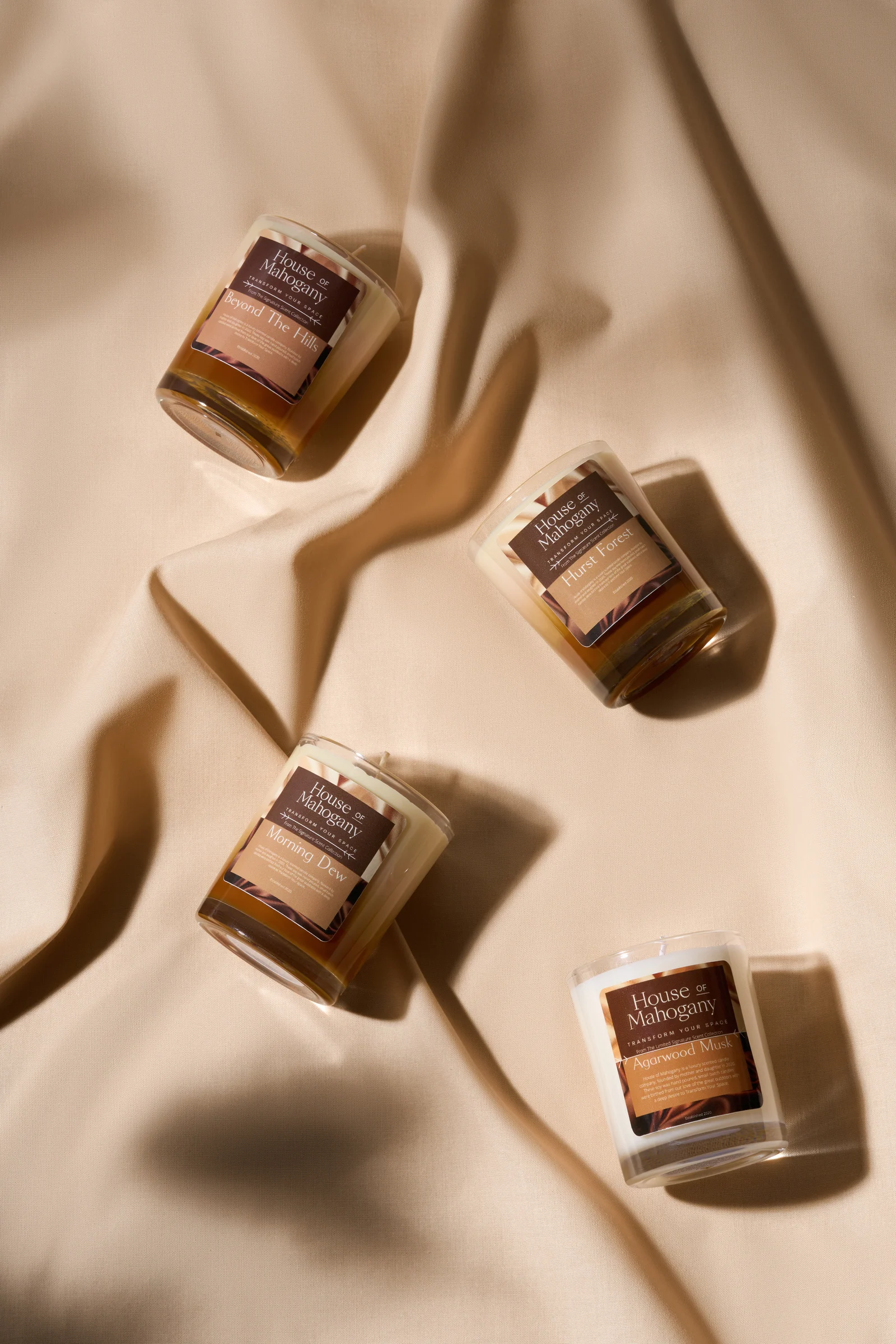 Four House of Mahogany candles arranged diagonally across folds of beige fabric.