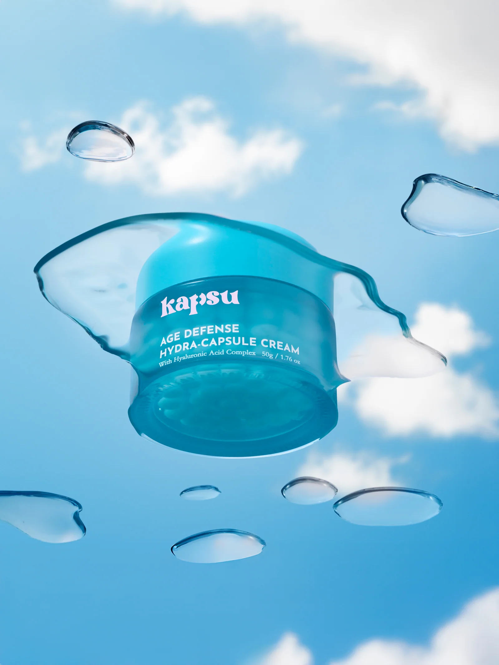 Turquoise Kapsu skincare jar suspended among clear gel droplets against a blue sky.