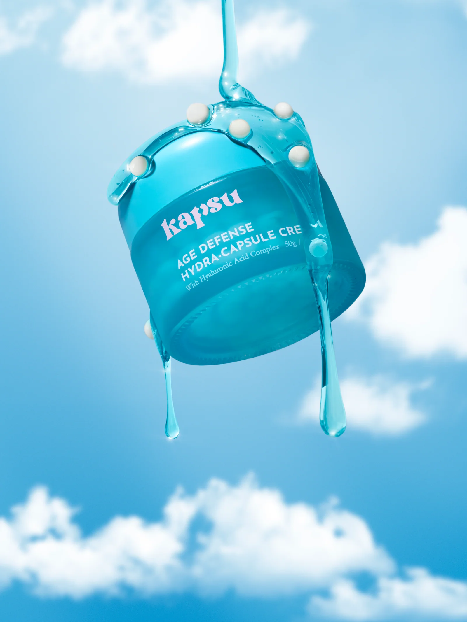 Close view of a Kapsu skincare jar coated in glossy blue gel against clouds.