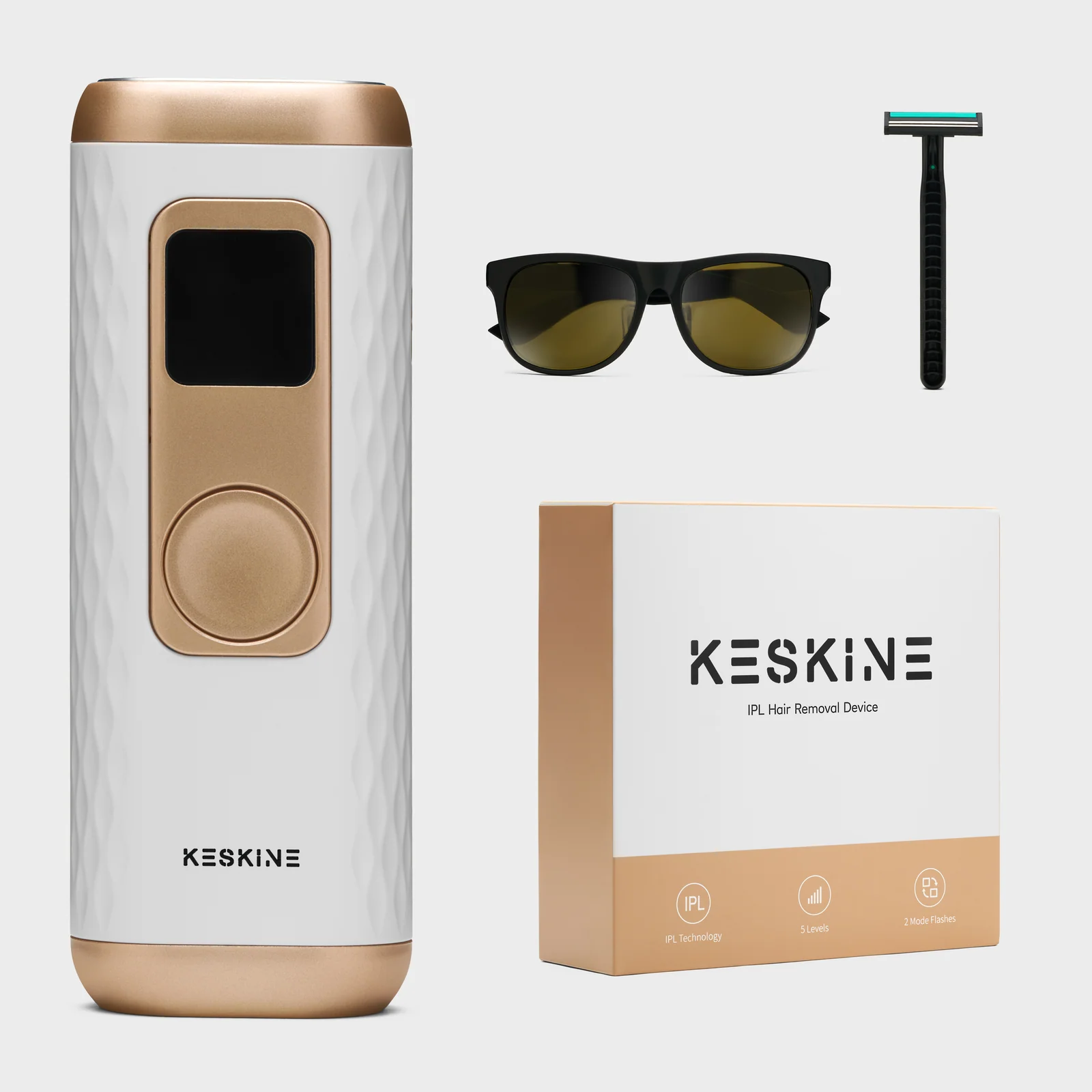 White and gold Keskine IPL hair-removal device with its box, dark glasses and razor against white.