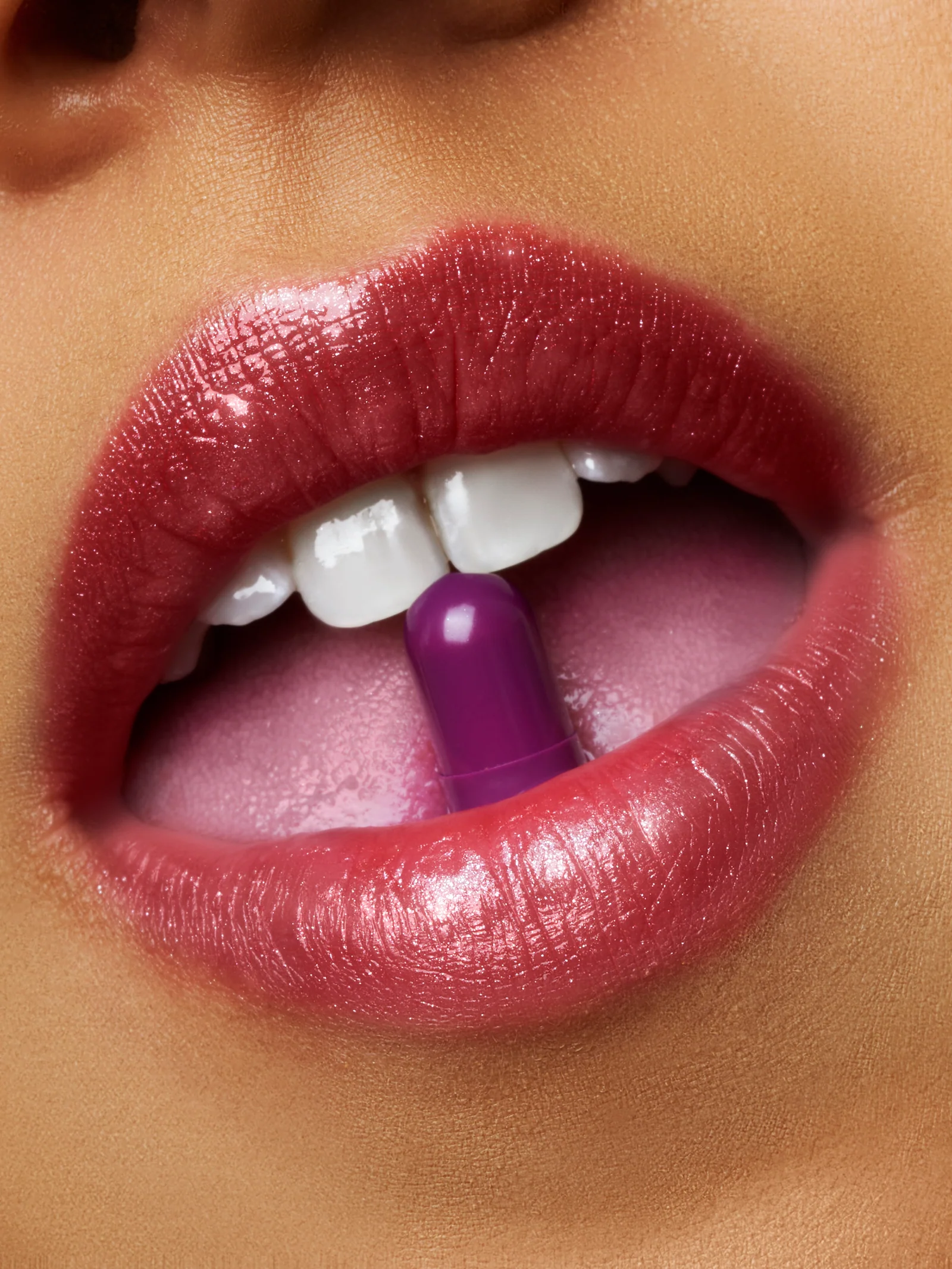 Close-up of red lips holding a purple supplement capsule between the teeth.
