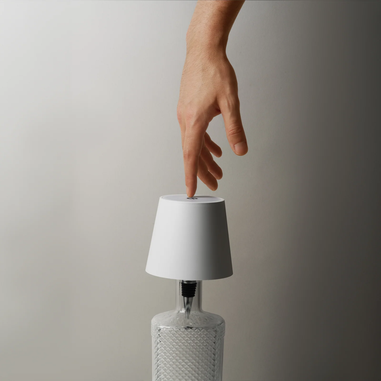 Hand touching the top of a white Liquor Lit lamp fitted to a clear textured bottle.