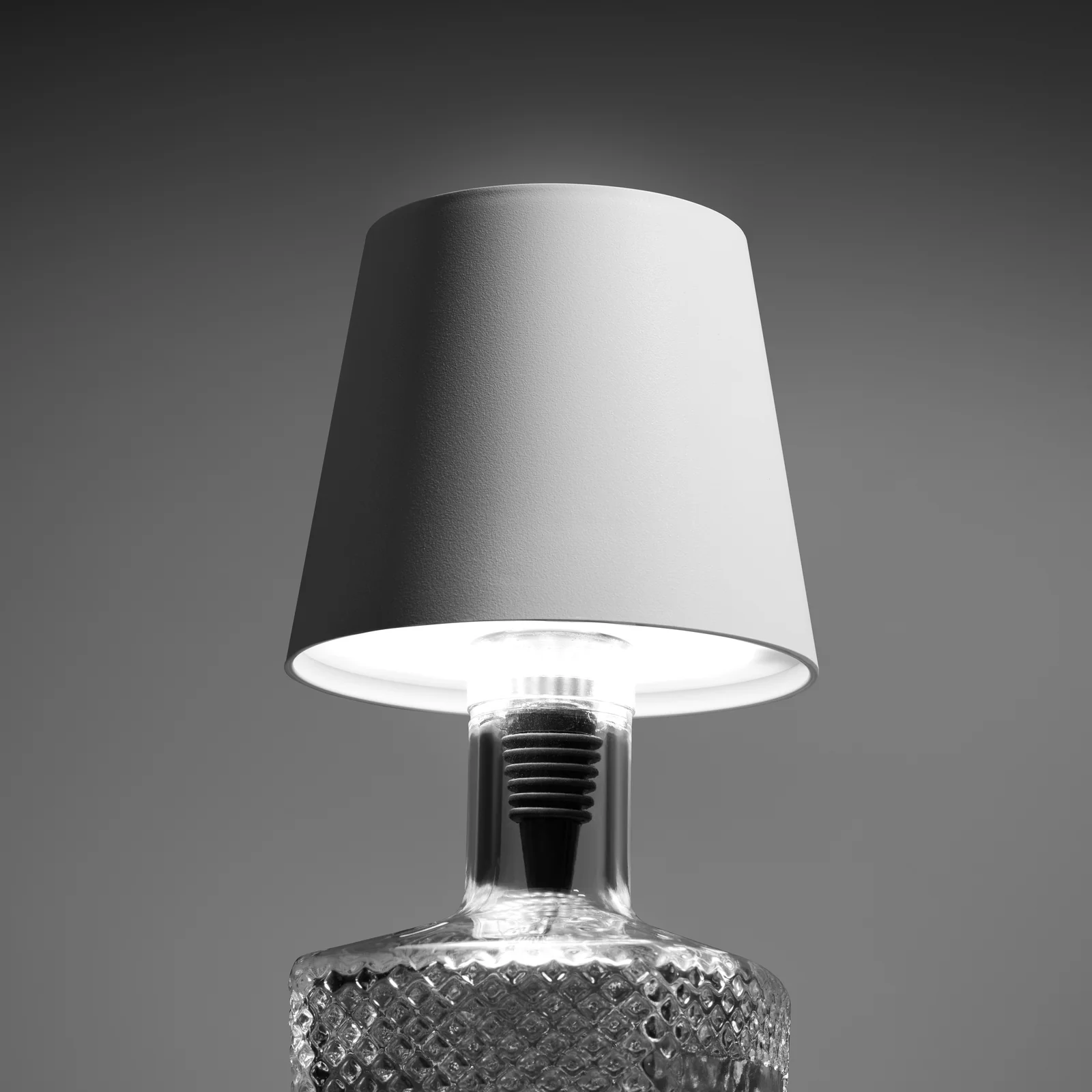 Close-up of an illuminated white Liquor Lit lamp top fitted to a textured bottle against grey.