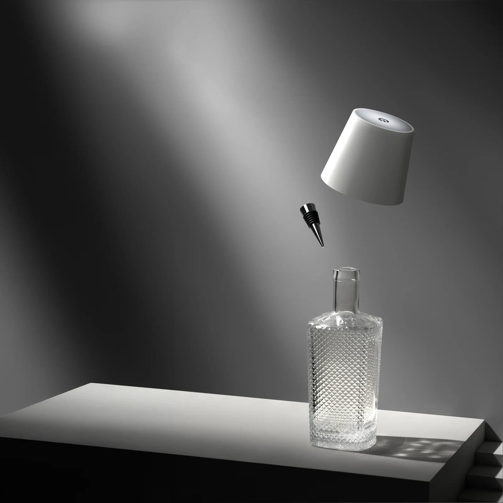 White Liquor Lit lamp top and bottle stopper suspended above a clear textured bottle on a grey platform.