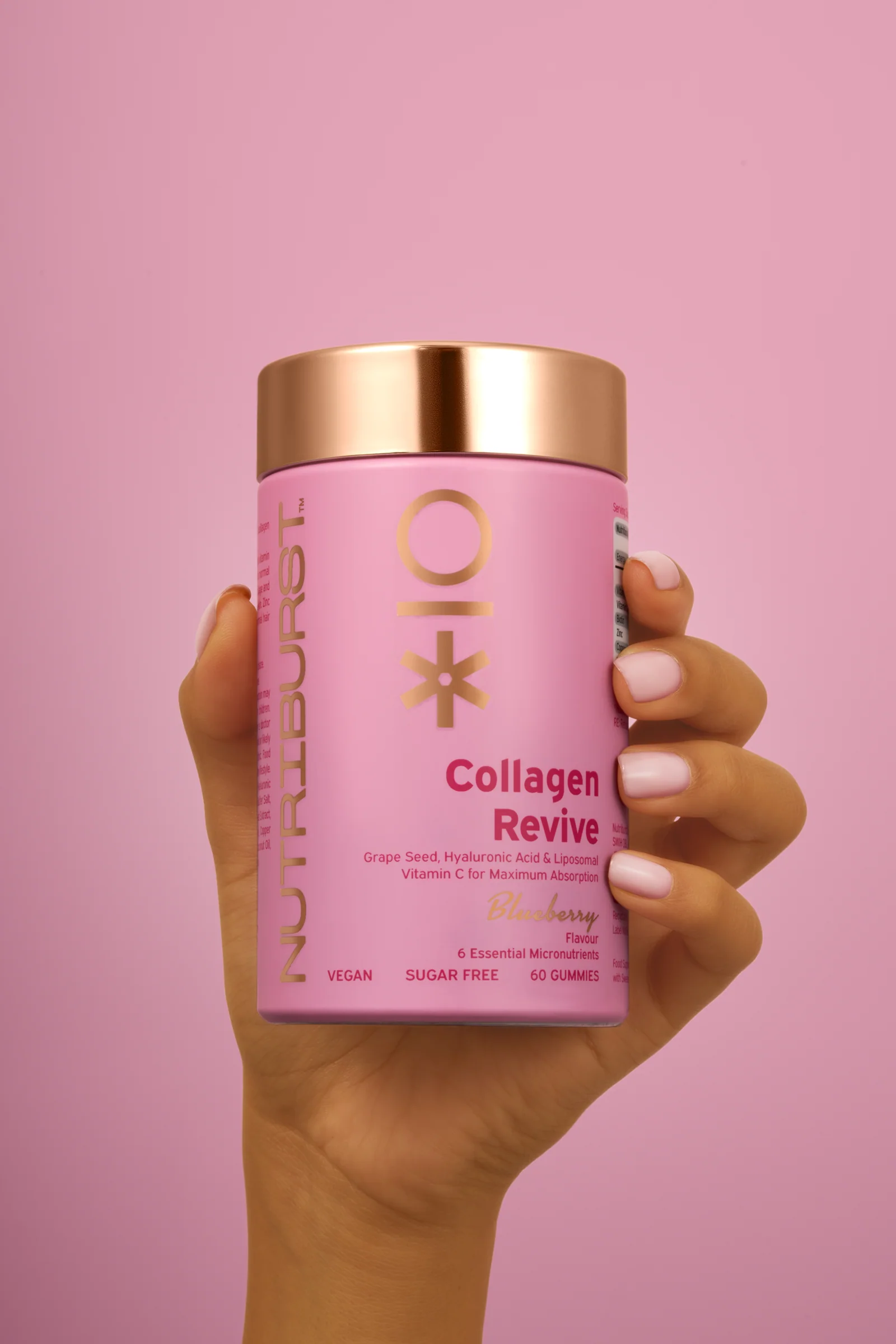 Hand holding a pink Nutriburst Collagen Revive jar against a pink background.