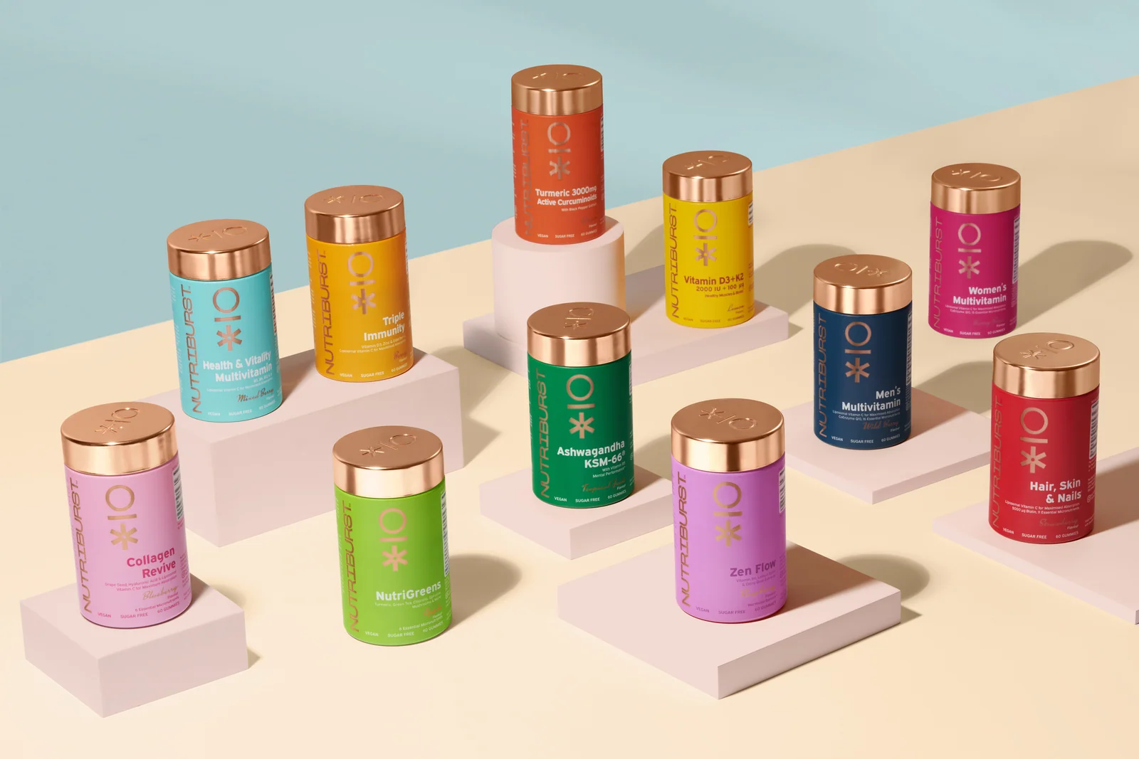 Colourful Nutriburst jars with copper-coloured lids arranged on pale pink platforms against cream and blue.