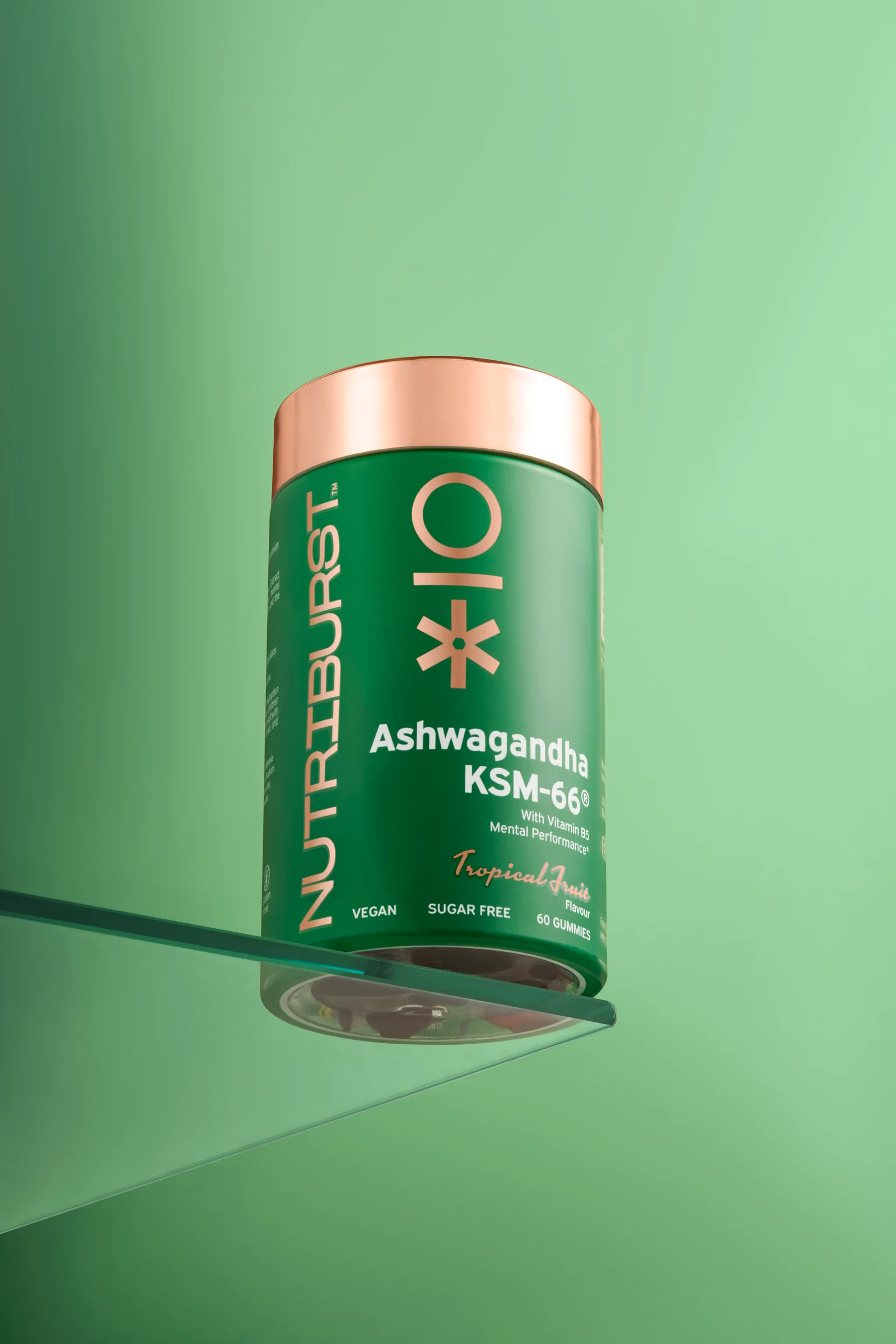 Green Nutriburst jar with a copper-coloured lid on a glass shelf against green.