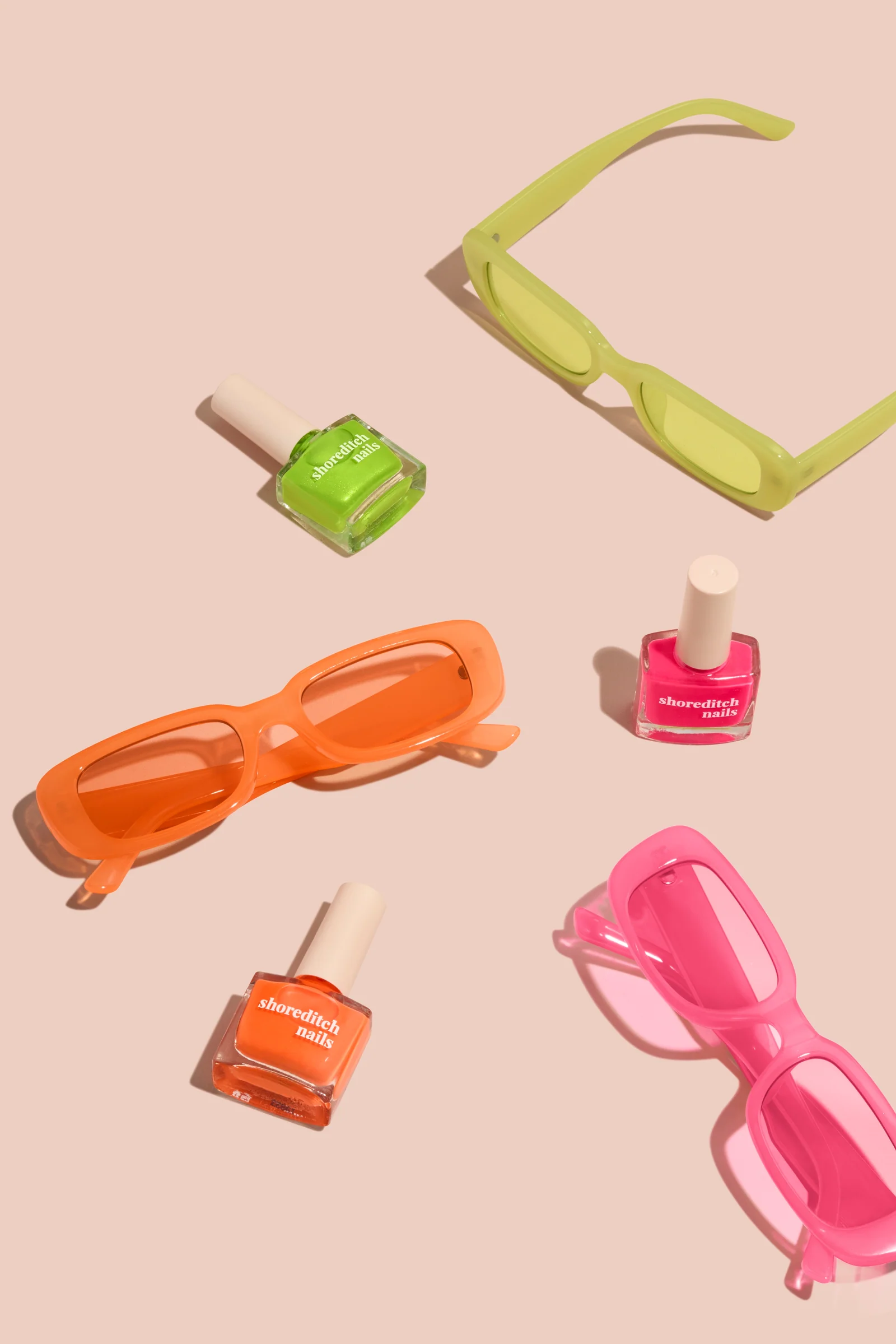 Green, orange and pink Shoreditch Nails polish bottles arranged with matching sunglasses on peach.