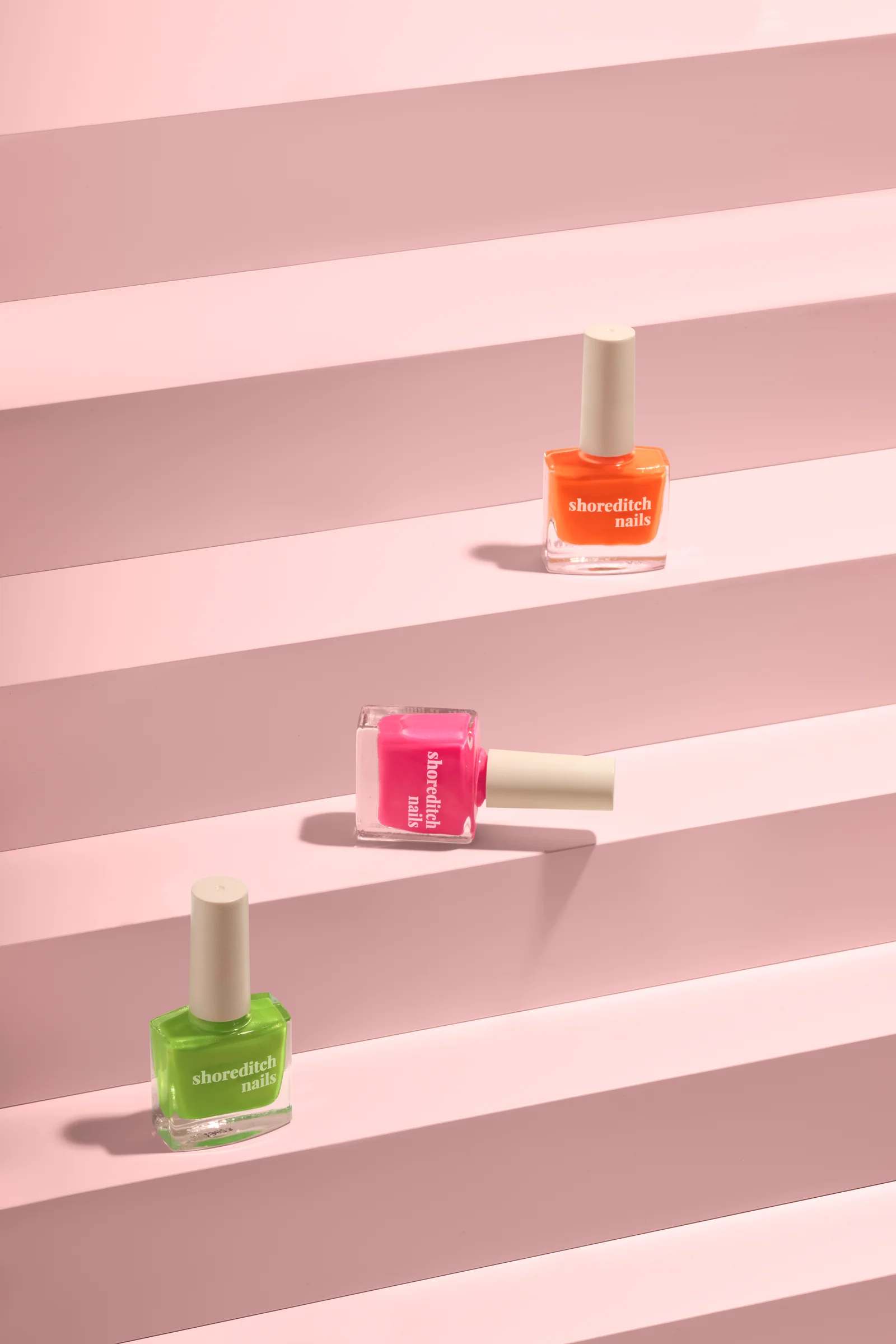 Green, pink and orange Shoreditch Nails polish bottles spaced along pink stepped platforms.