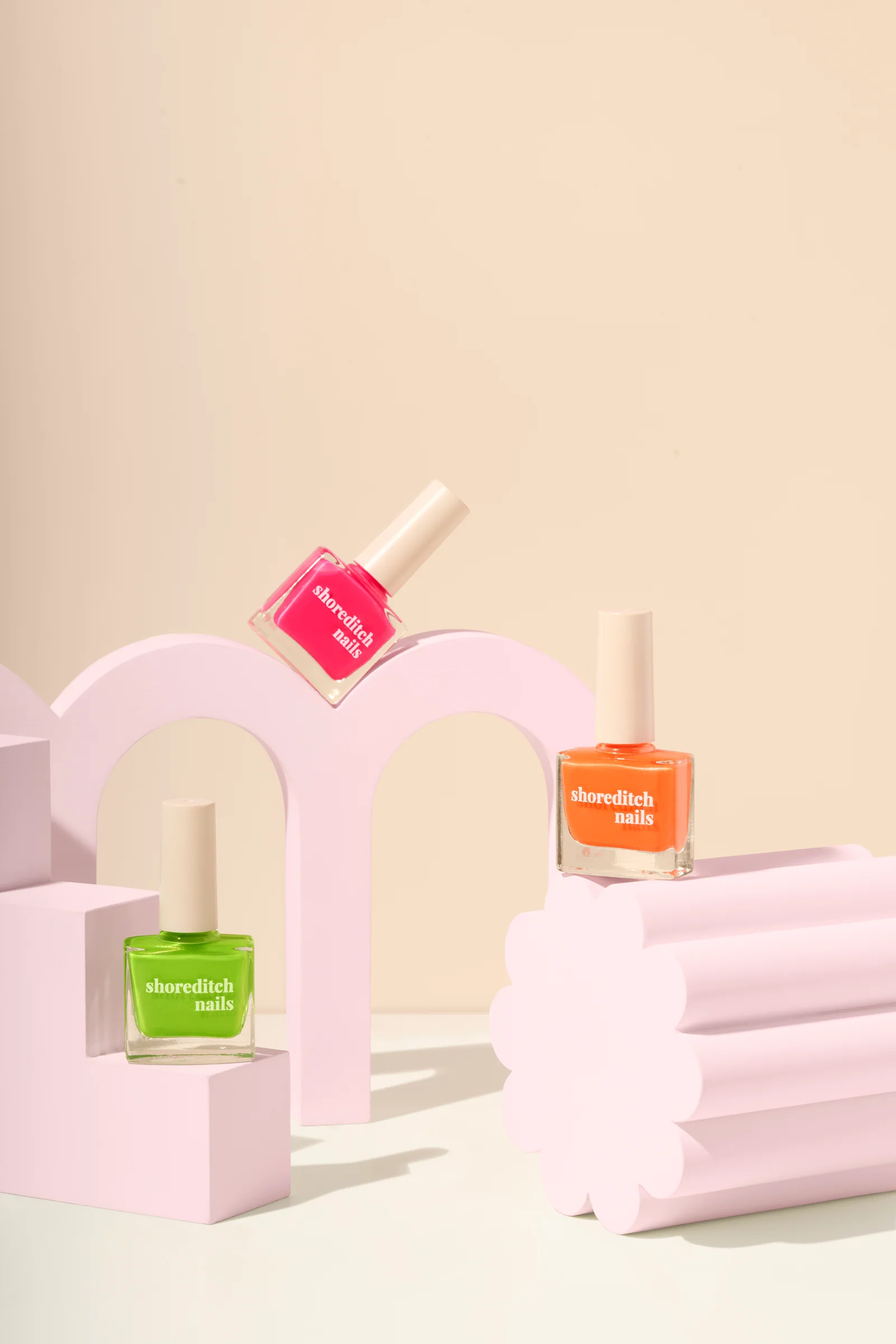 Shoreditch Nails polish bottles arranged on pink arch and fluted display props against peach.