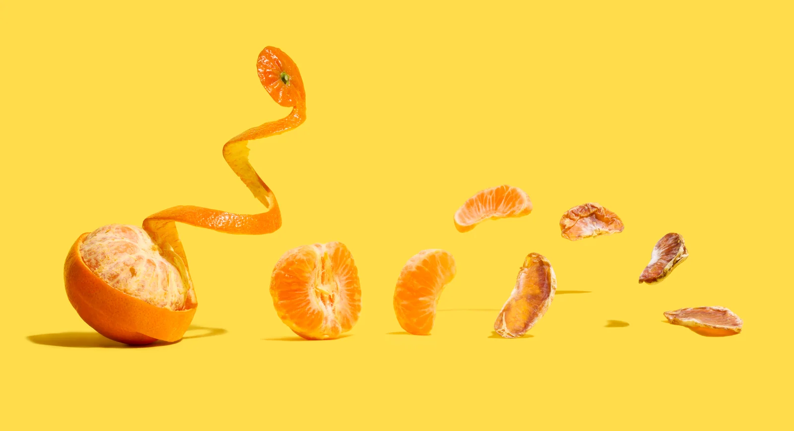 Fresh mandarin, curled peel, segments and dried slices arranged across a yellow background.