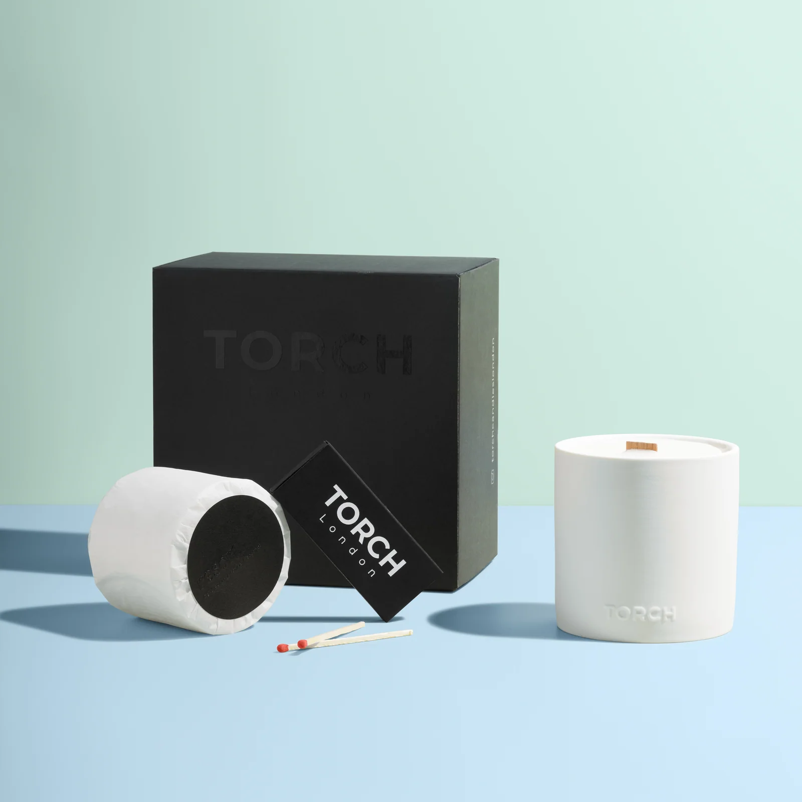 White Torch candle, wrapped refill, matches and matchbox beside a black presentation box on a blue-and-green set.