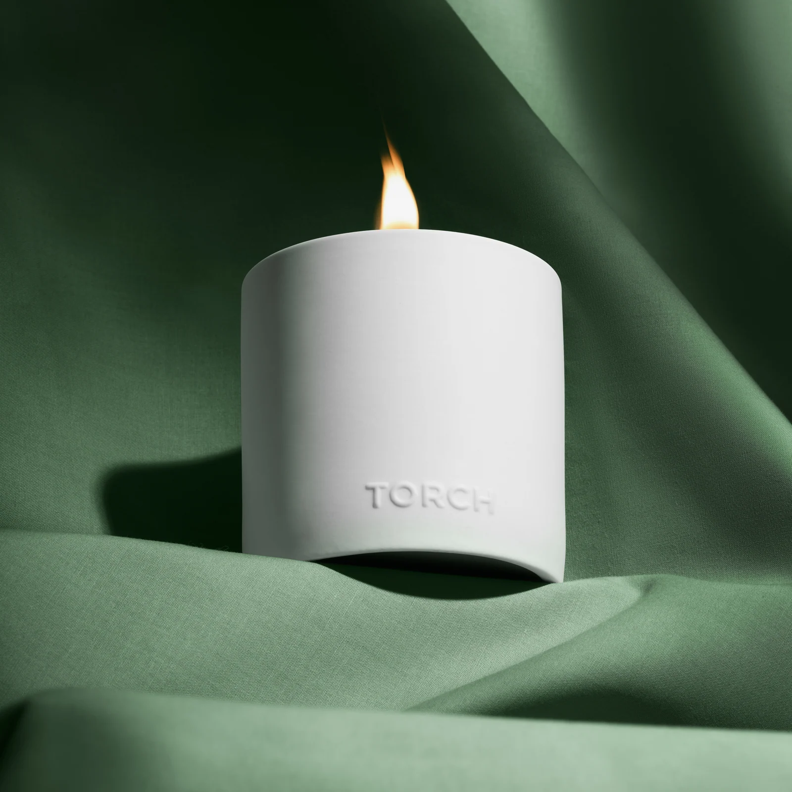 Lit white Torch candle nestled in folds of green fabric.