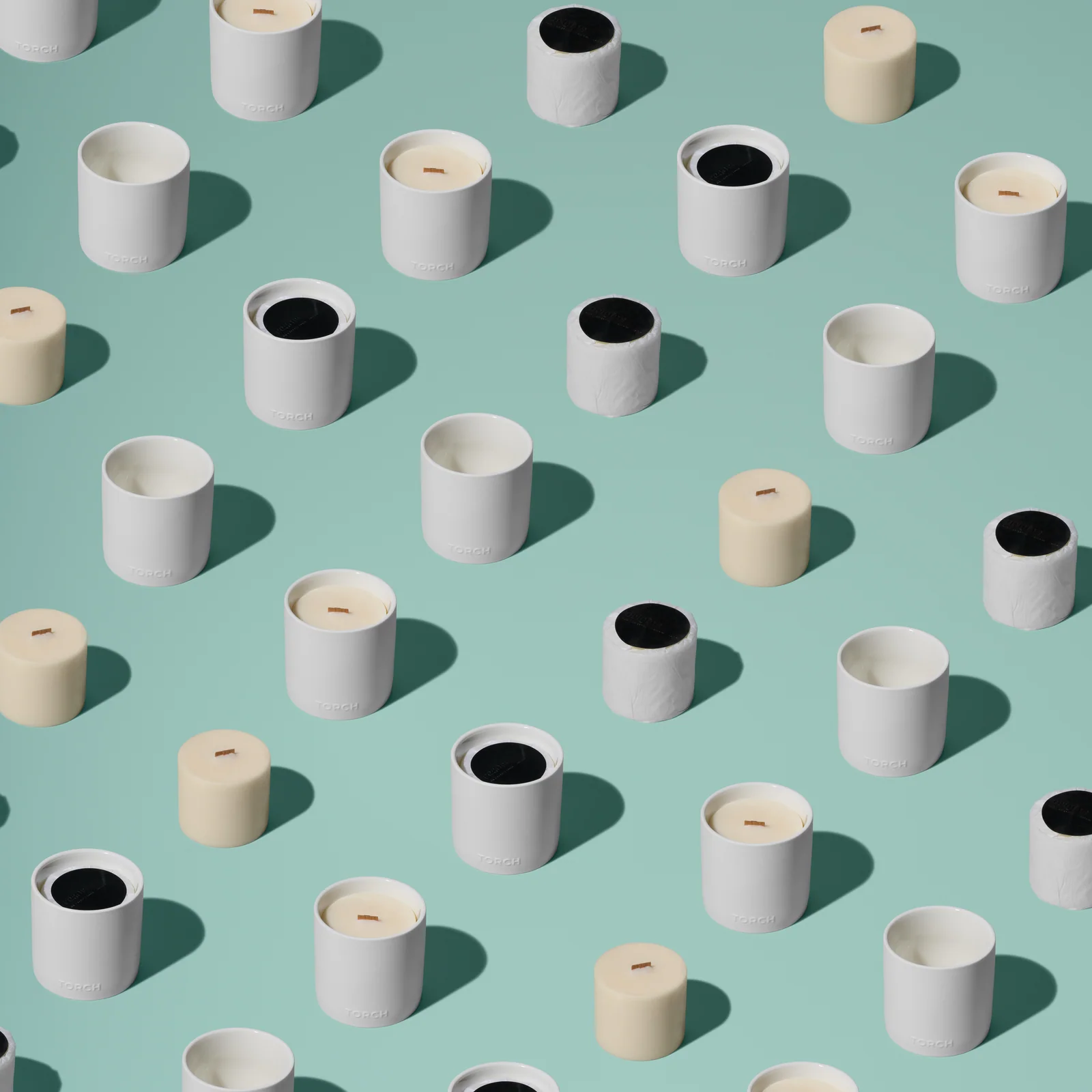 White Torch vessels, wrapped refills and bare wax candles arranged in repeating rows against green.