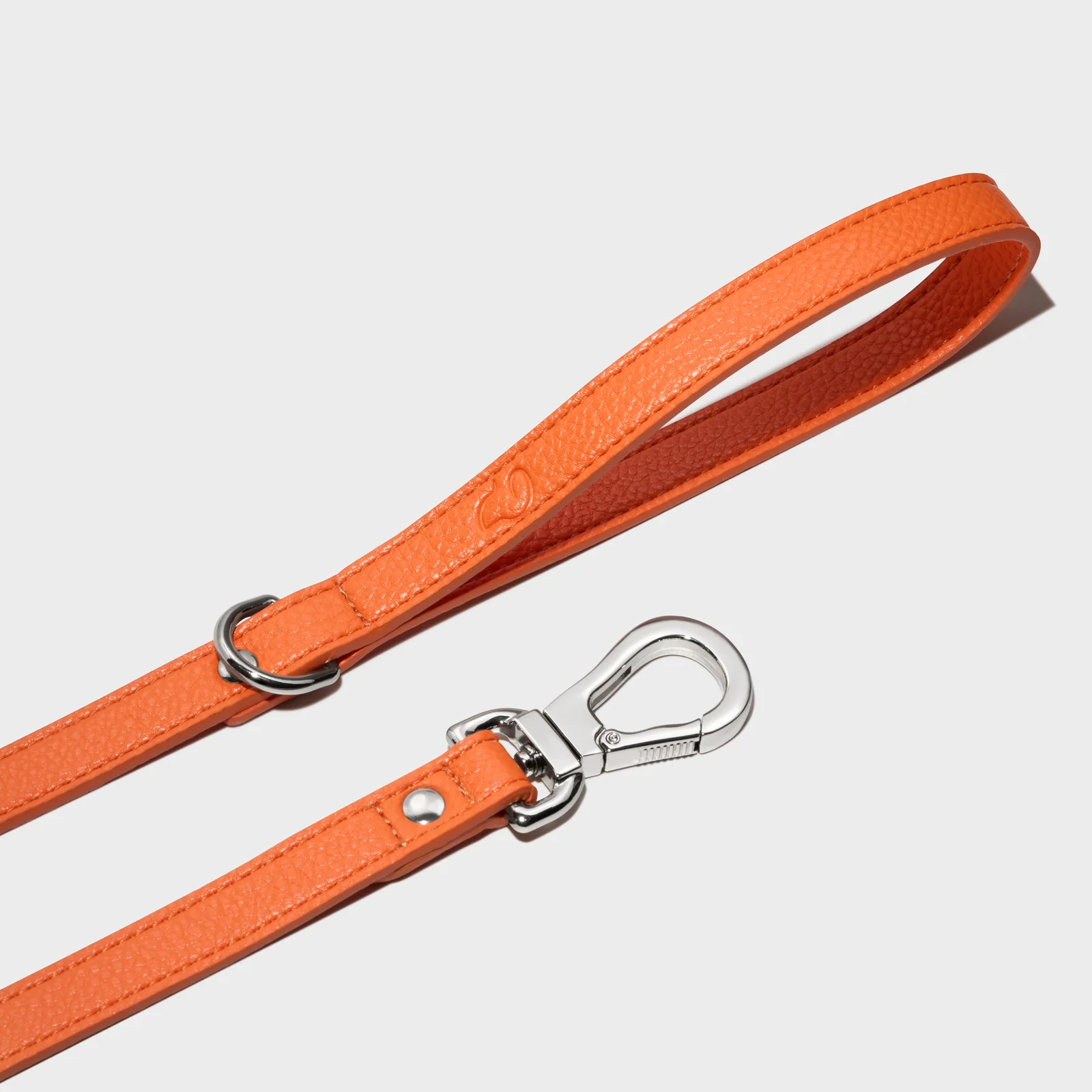 Orange Truffle and Paw leather lead with polished metal hardware on a grey background.