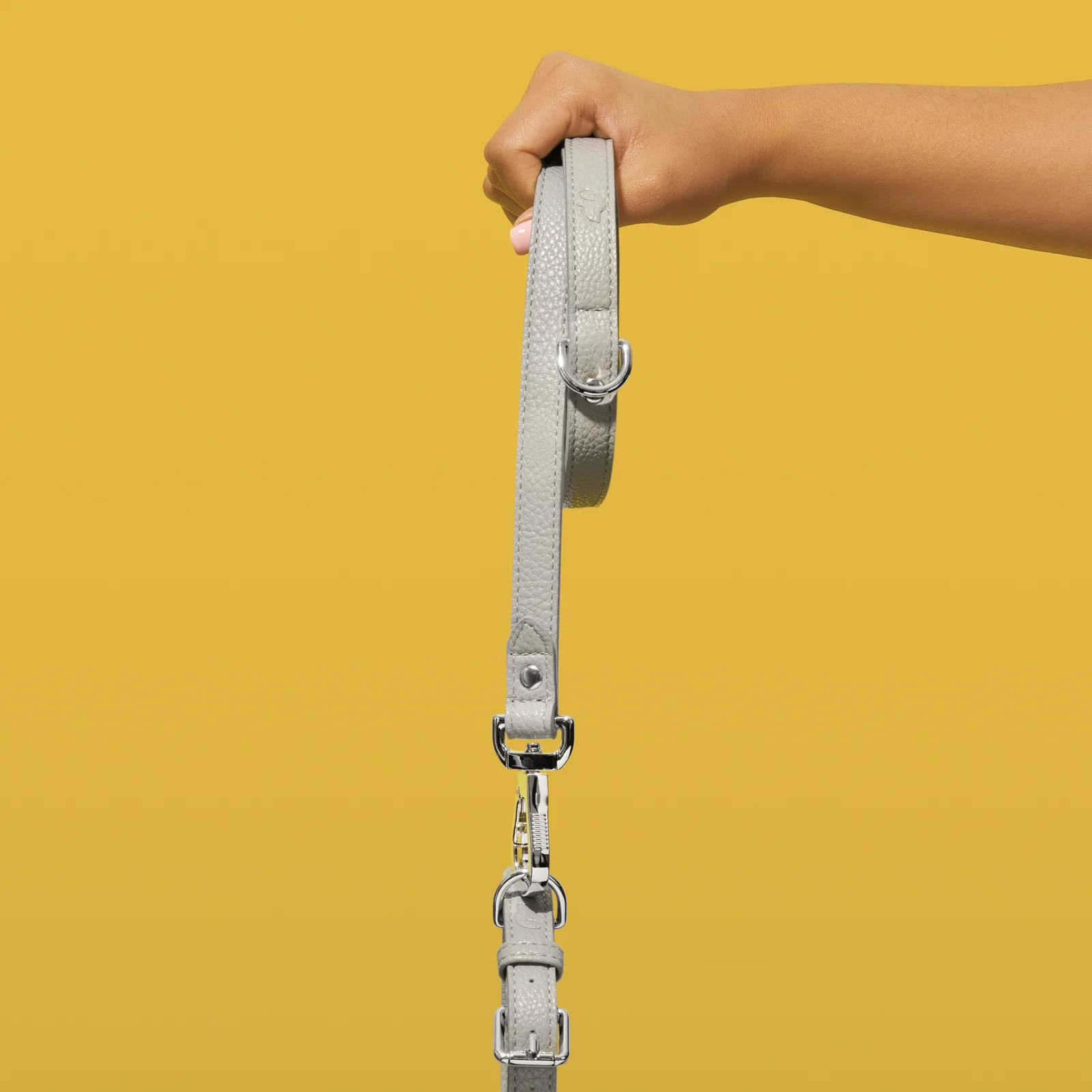 Hand holding a grey Truffle and Paw leather lead against yellow.