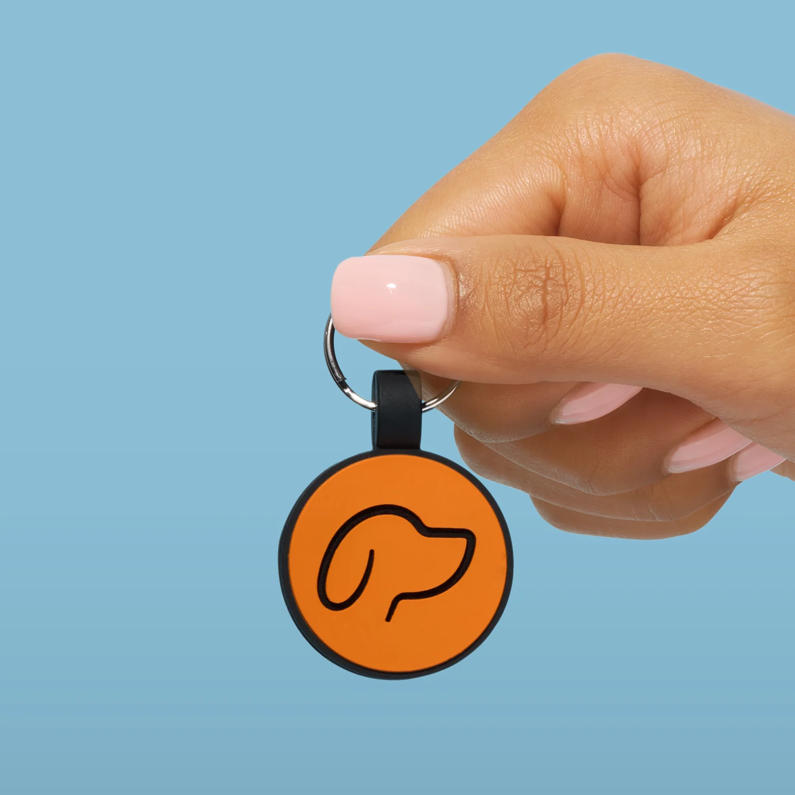 Hand holding a round orange Truffle and Paw tag with a dog-head outline against blue.