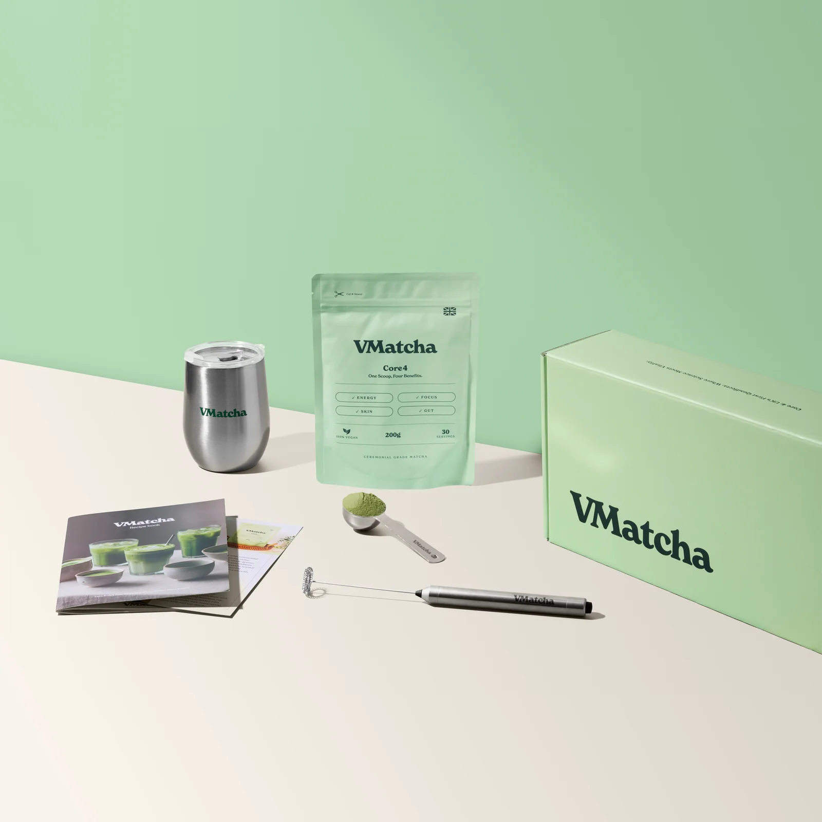 VMatcha Core4 pouch, branded cup, scoop and whisk beside a presentation box and recipe booklet on a cream-and-green set.