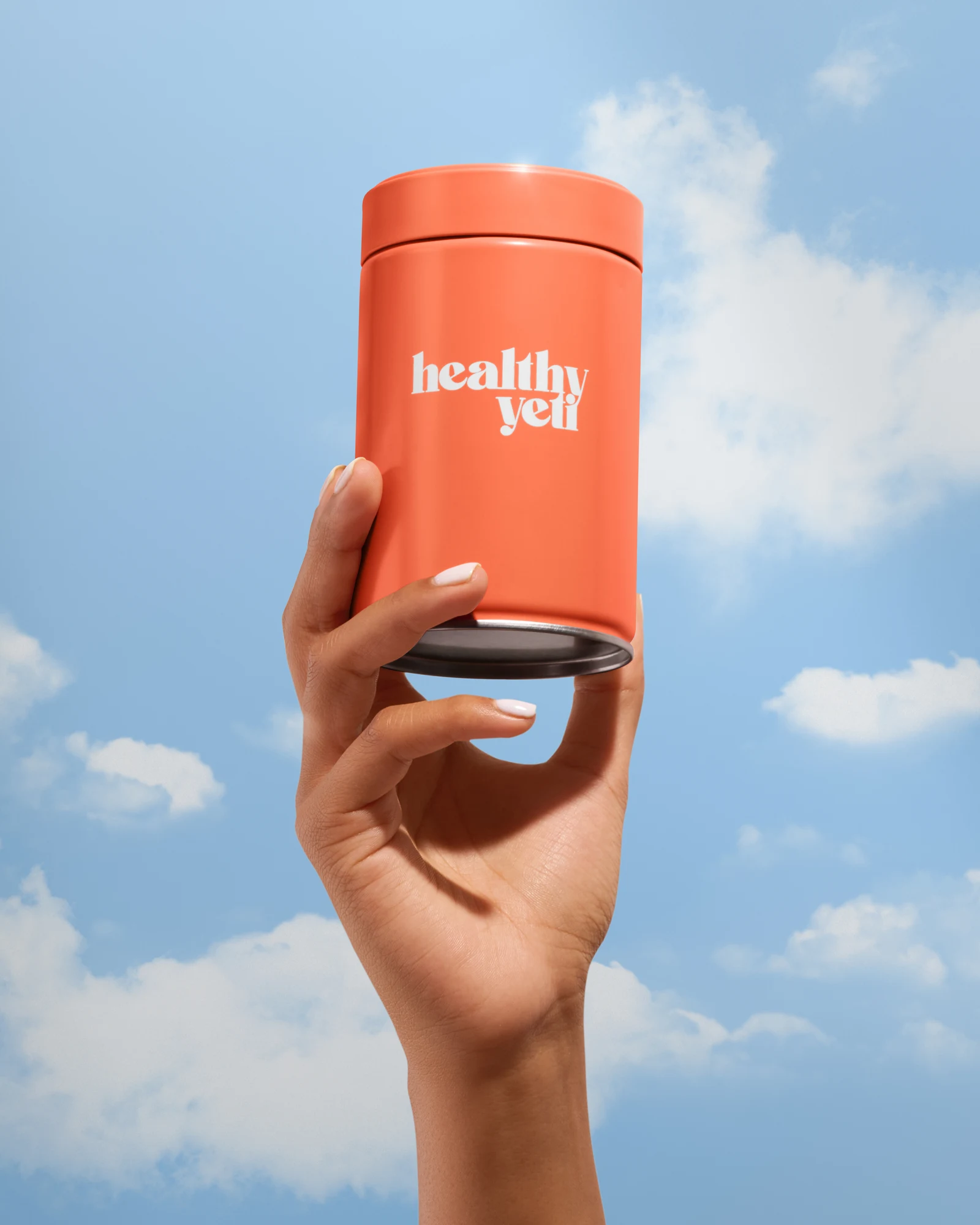 Hand holding an orange Healthy Yeti jar against a blue sky with clouds.
