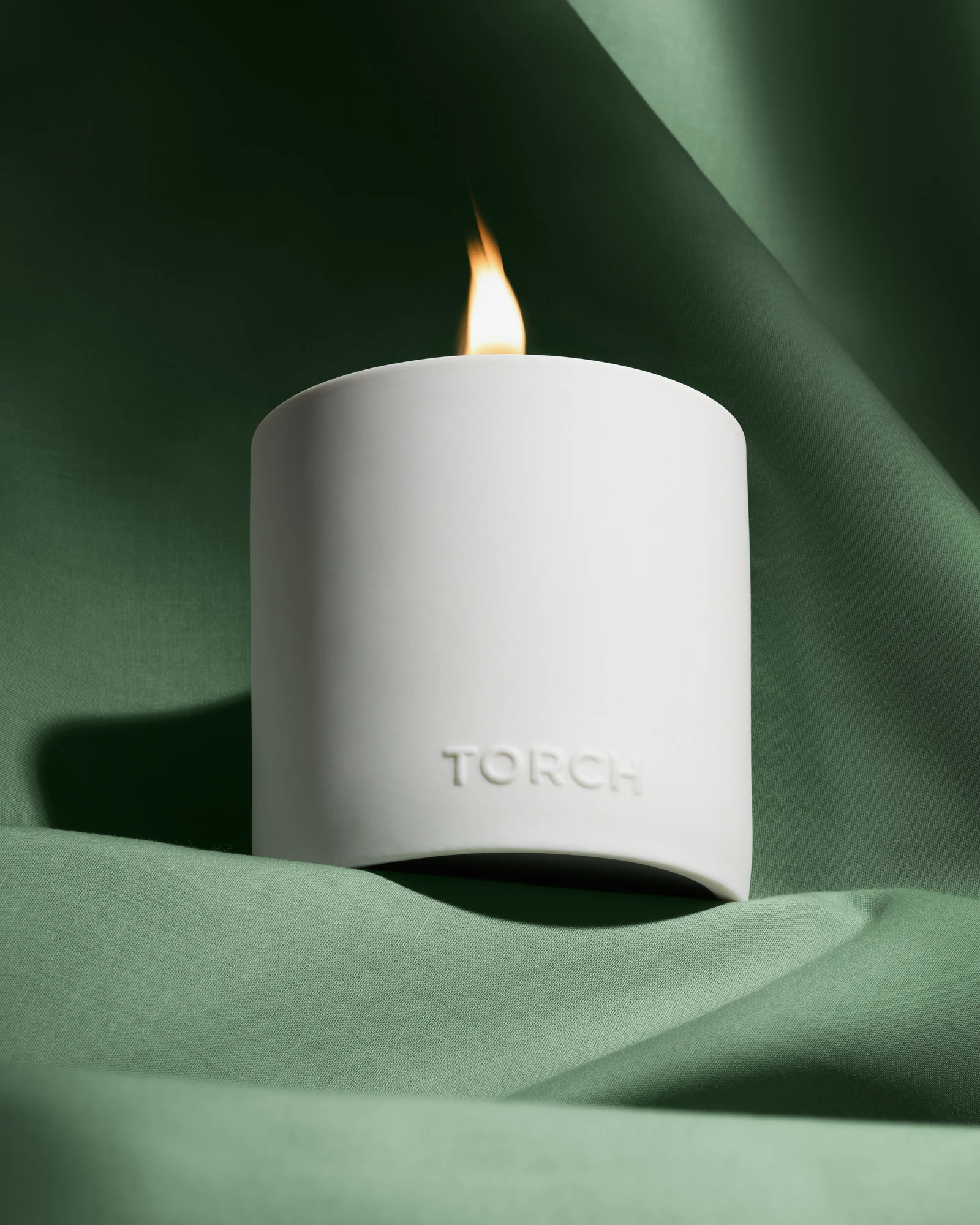 Lit white Torch candle on green fabric with directional light and shadows.